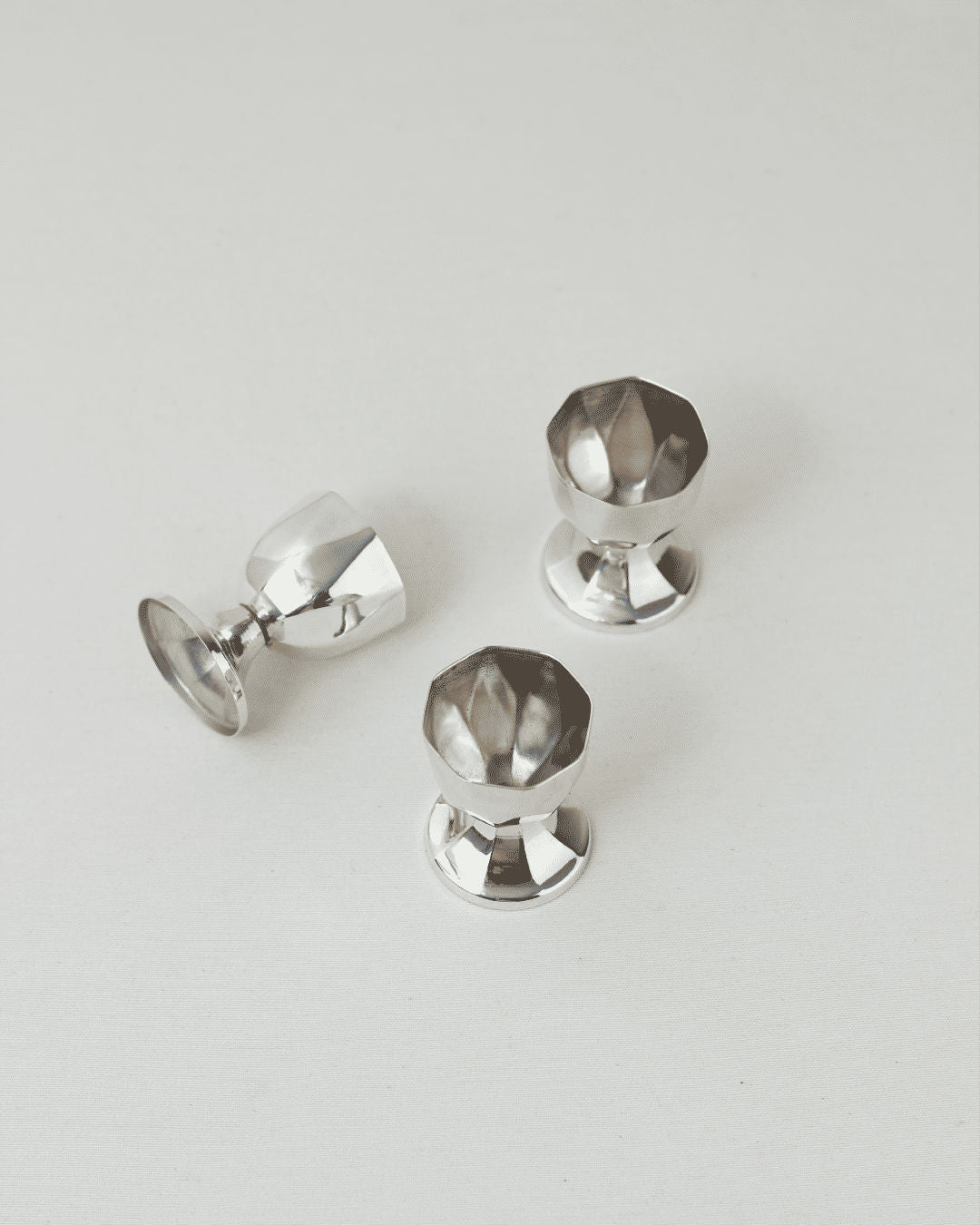 Three polished silver egg cups with faceted crystal tops arranged on white surface