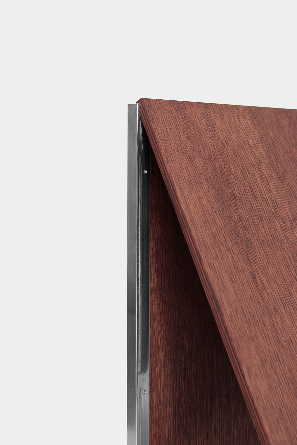 Close-up of the Lounge Chair 2022 by Studio HAOS: a wooden panel with a reddish-brown finish, accented by a sleek metal strip, set against a light gray background—highlighting the brand's grounded elegance through humble materials.