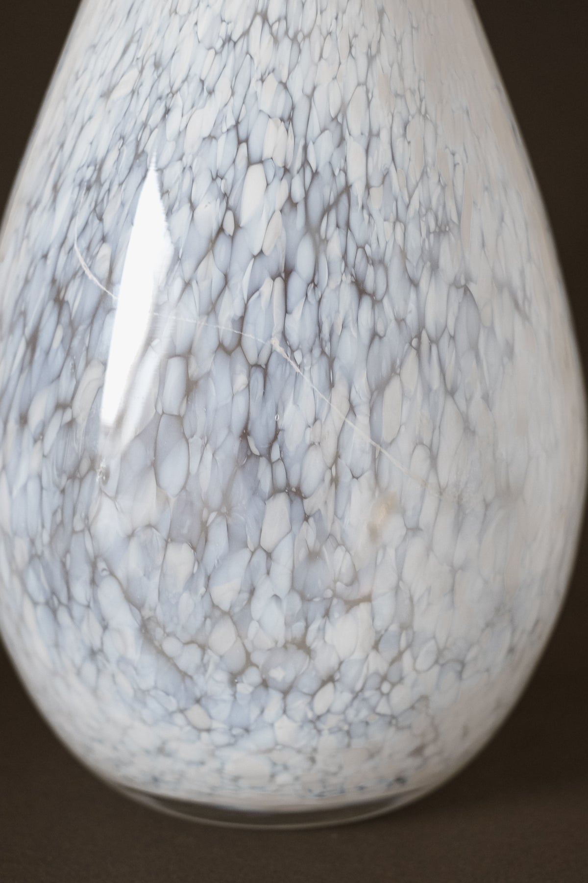 A close-up of the White Vase Tortoise Glass by septembre studios, showcasing its pear-shaped form, marbled white and gray speckles, smooth surface, and glossy finish that reflects light for a distinctive look.