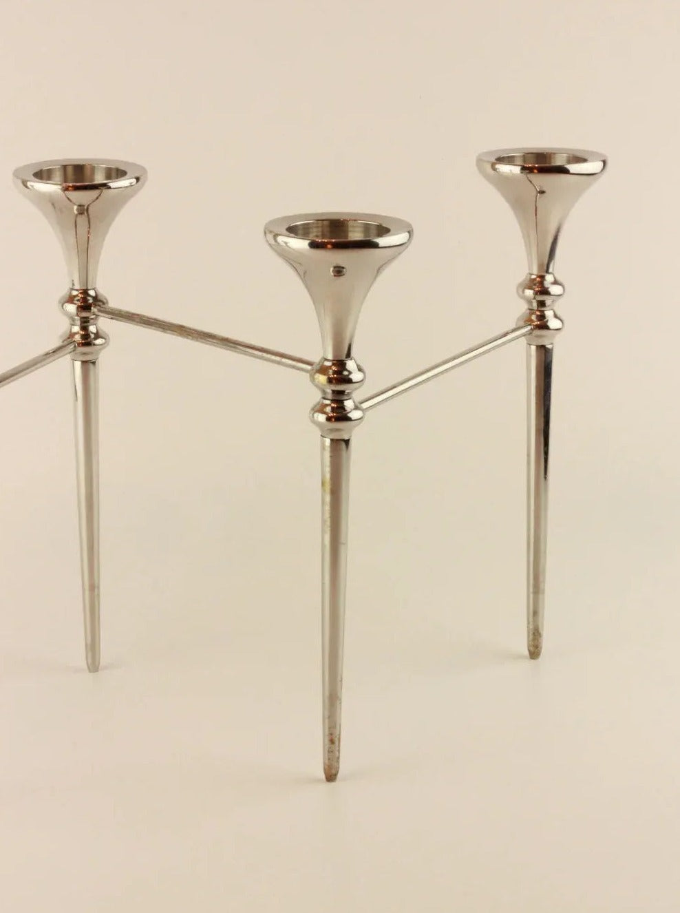 A Scandinavian Modular Candelabra by Boga Avante Shop, silver with sleek, modular arms and a modern design reminiscent of a vintage chrome chandelier. Each prong holds a single candle, and the structure is connected by horizontal rods near the top. The holder stands on three pointed legs.