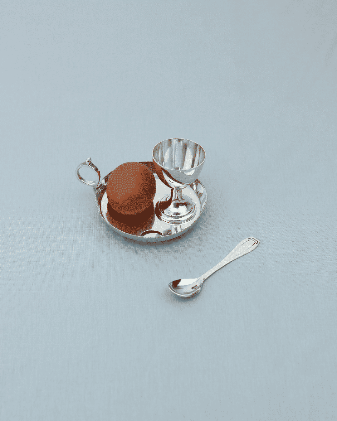 Silver egg cup set with tray and spoon on neutral background