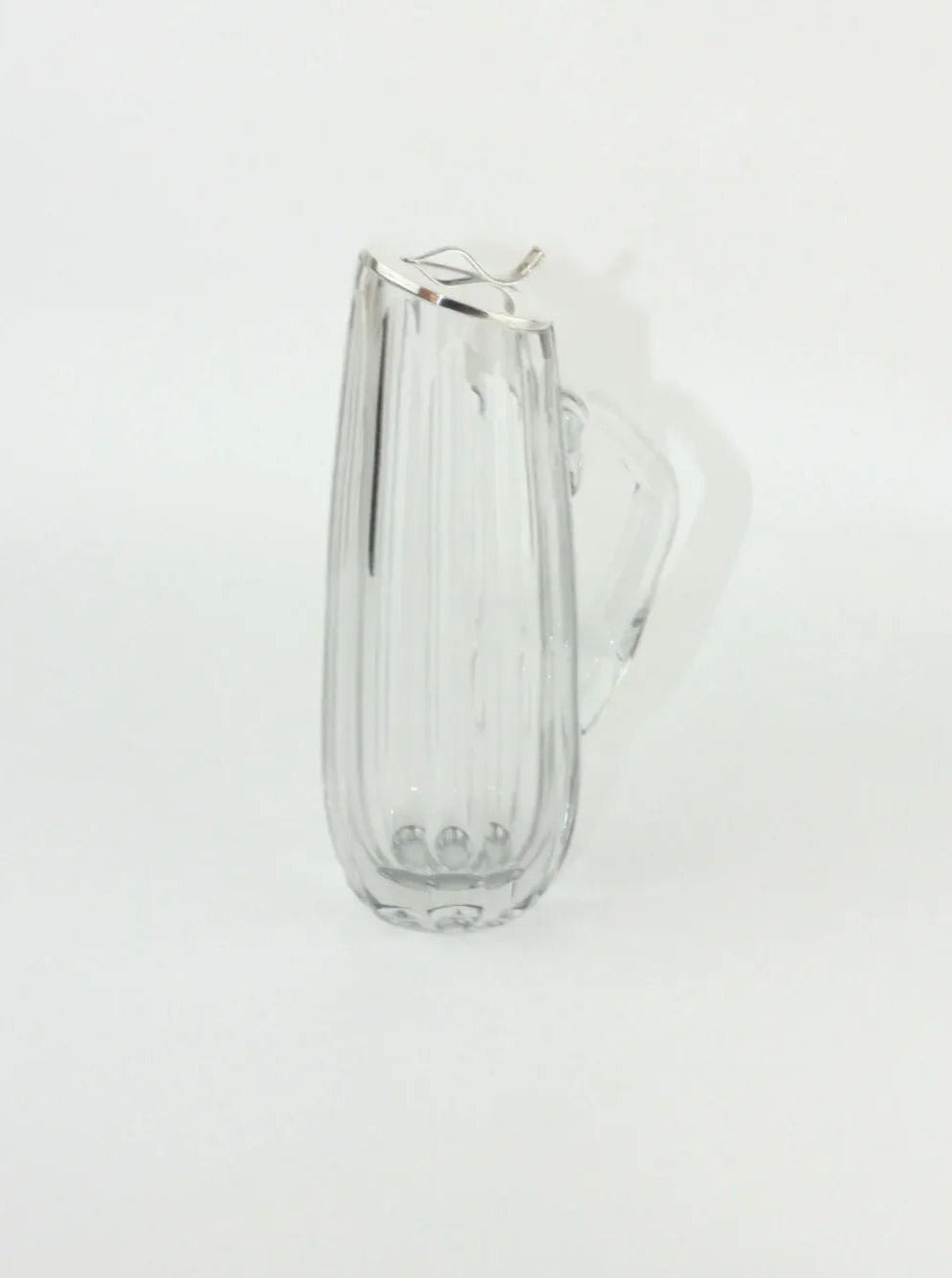 A Boga Avante Shop Crystal Decanter with a vertically ribbed design and a handle sits against a plain white background. Reminiscent of vintage crystalware, it features a narrow spout for pouring and casts a faint shadow on the surface.