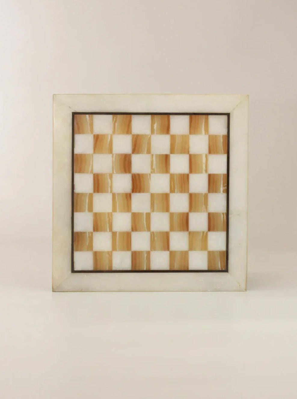 The Boga Avante Shop Vintage Marble Chessboard, crafted from marble stone, showcases a square design with alternating light brown and white squares. The chessboard is bordered by a light grey marble frame and is situated on a neutral background.