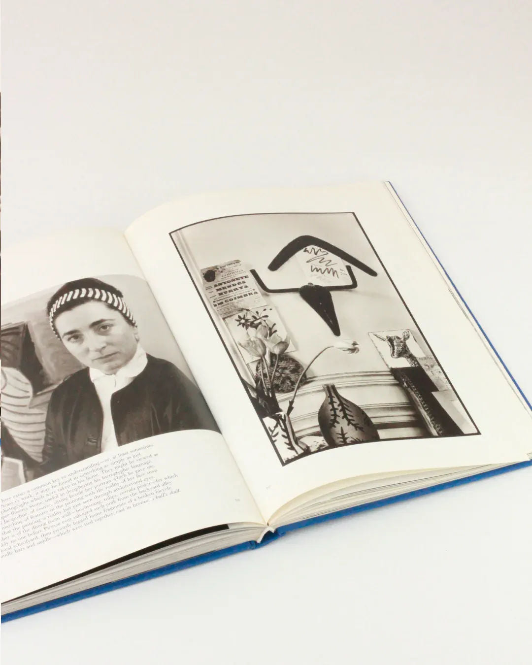 An open book displaying two black-and-white photos. The left page features an intimate portrait of a person with a headband, reminiscent of Picasso and Jacqueline, while the right page shows a wall decorated with various objects, including a bird-shaped figure and a plant. The book "Picasso and Jacqueline" by Boga Avante Shop is set on a white surface.
