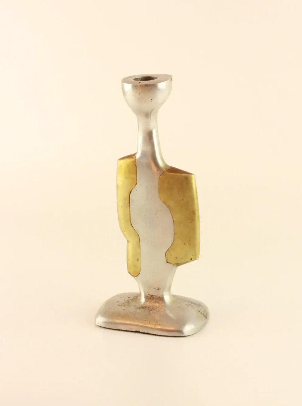 A silver metallic Brutalist Candleholders by Boga Avante Shop with a modern, abstract design. It features golden accents on both sides of its slender, elongated body and has a flat, asymmetrical base reminiscent of David Marshall's aluminum and brass works. The background is plain white.