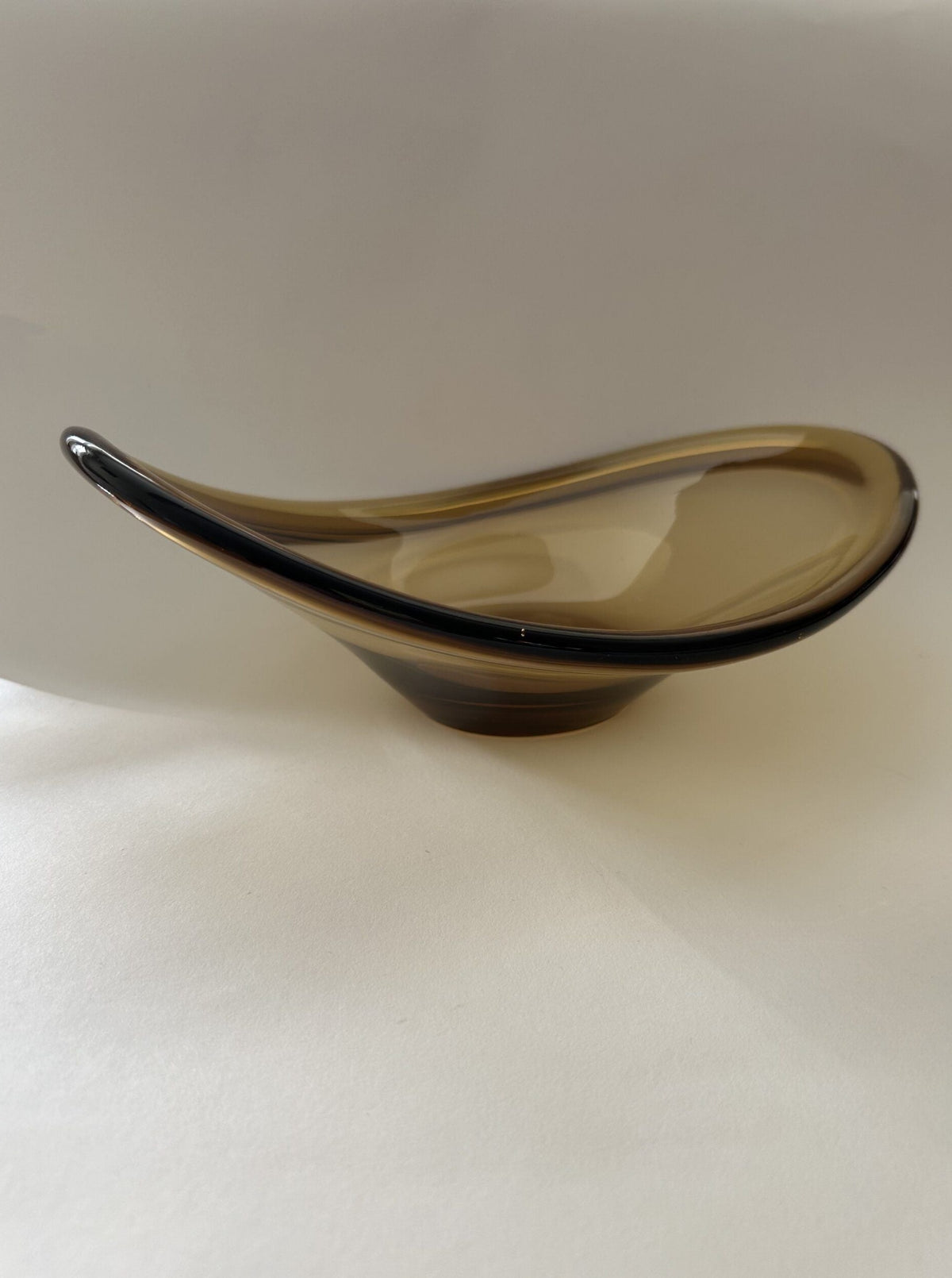 Introducing the Vintage Italian Murano Glass Dish by Flock Studio: a curved, sleek piece with a modern design. It boasts a translucent amber hue with a smooth, polished surface and rests elegantly on a light background, highlighting its exquisite asymmetrical shape.
