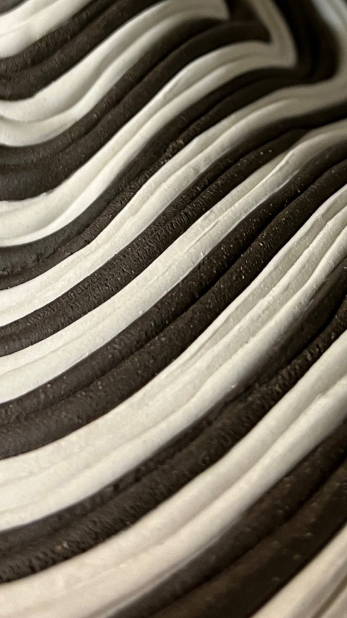 A close-up of The Soucy Shop's Black & White Bottle reveals undulating black and white wavy lines that evoke stoneware coils. Resembling a topographical map or layered fabric, these curves impart depth and movement across the surface.
