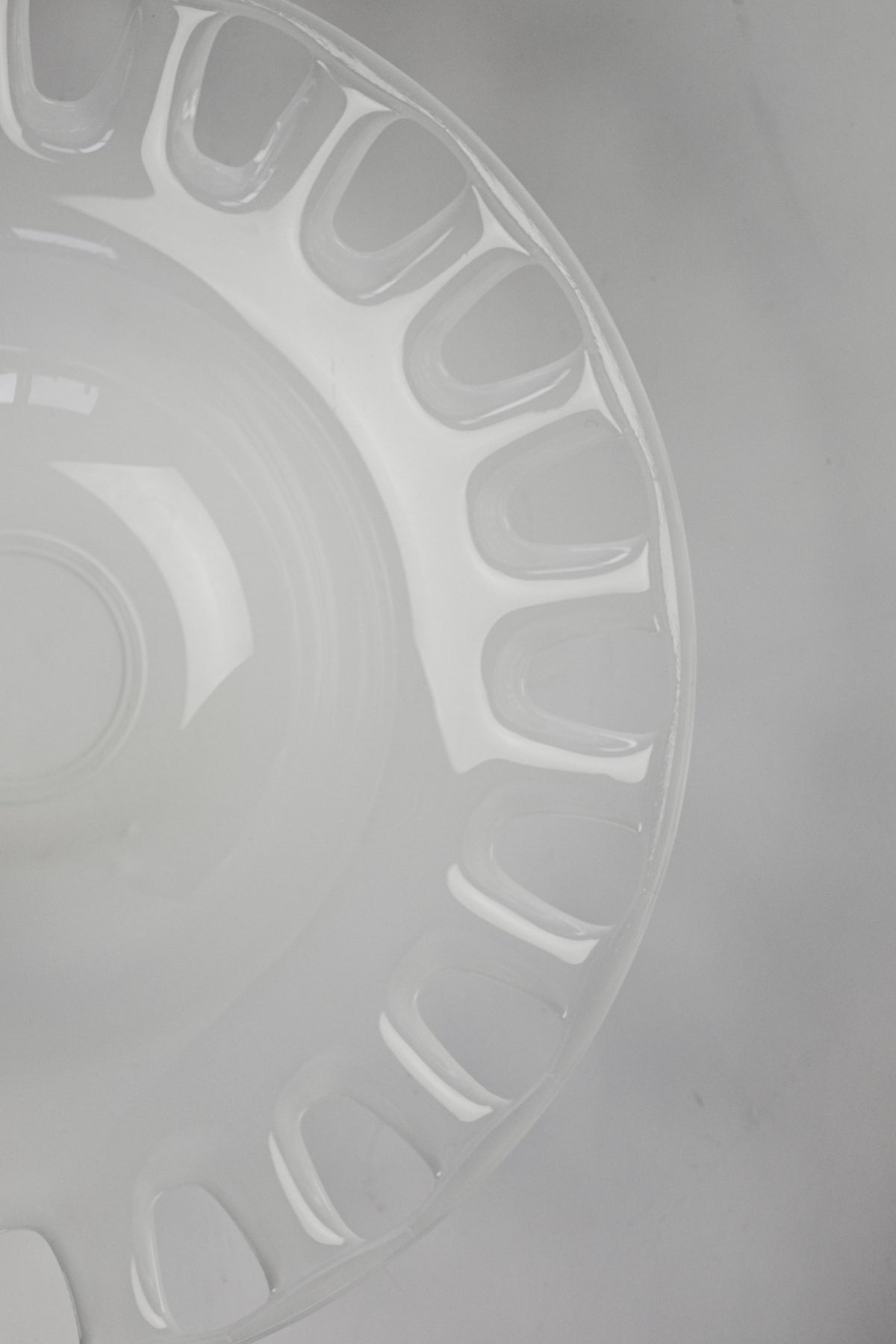 The Large Bowl of Milk Glass from septembre studios features a clear, empty design with scalloped edges and small, rounded curves. Its glossy finish gracefully catches light against the gray background, emphasizing its transparent texture and simple aesthetic.
