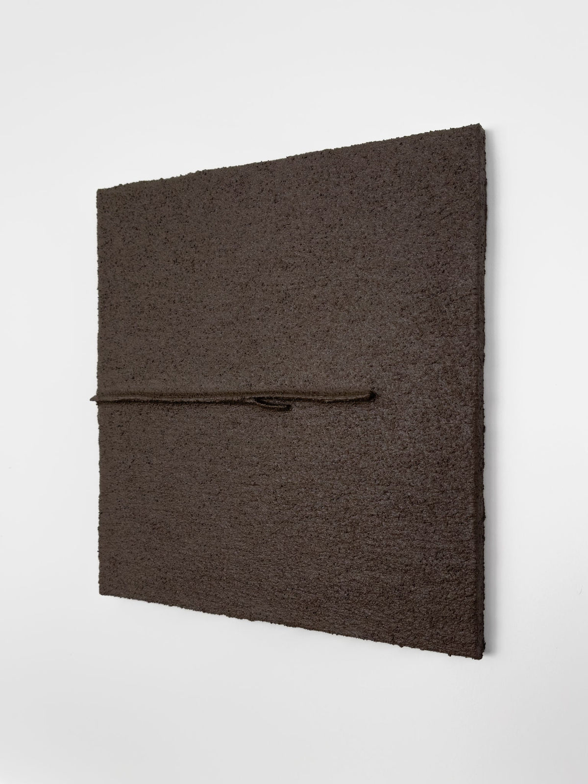 Shadow World 03" by Delal Salazar is a textured, dark brown square artwork with acrylic and sand on canvas. Mounted on a white wall, it features a thin brown cord embedded off-center, enhancing the piece's three-dimensional depth.