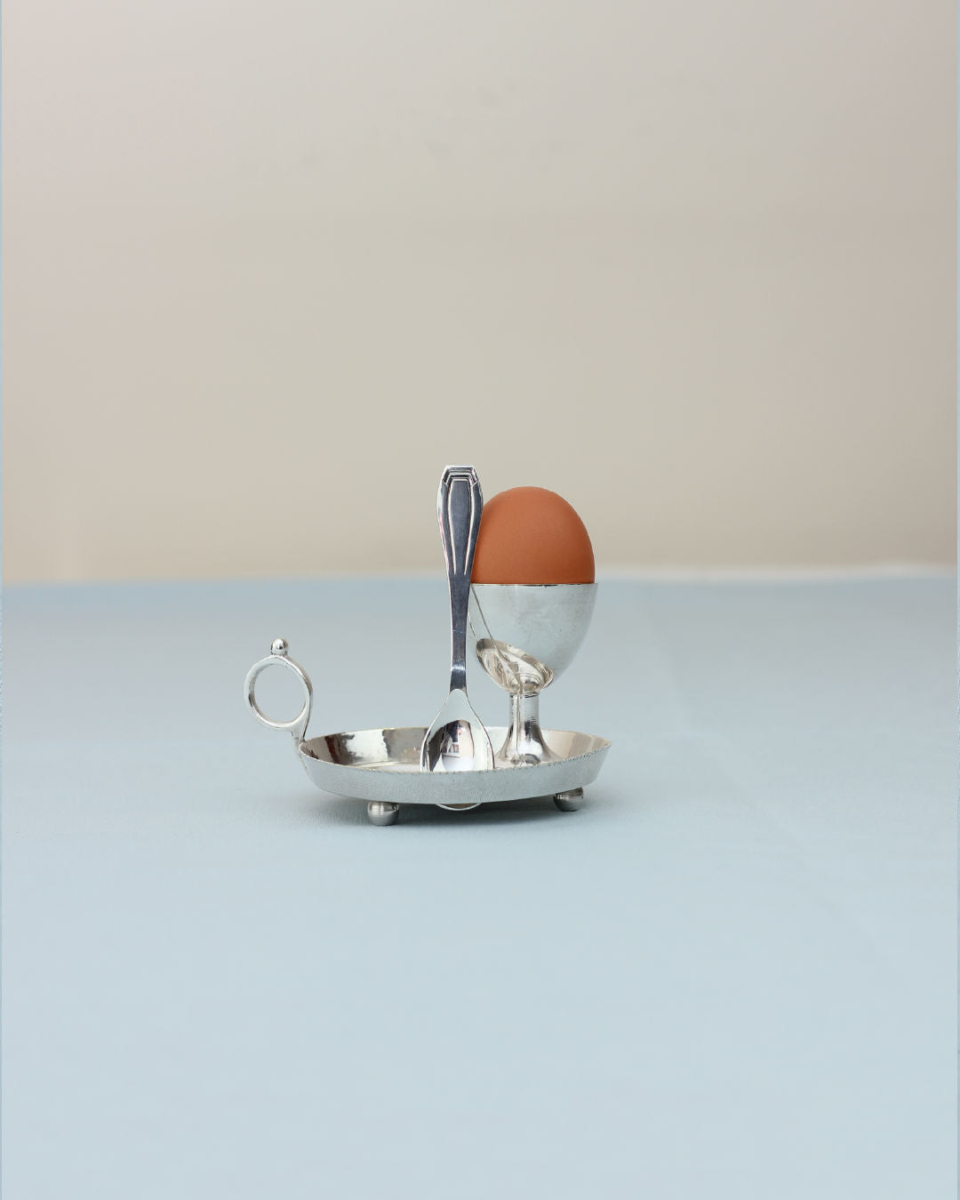 Silver egg cup with spoon on oval tray, brown egg displayed
