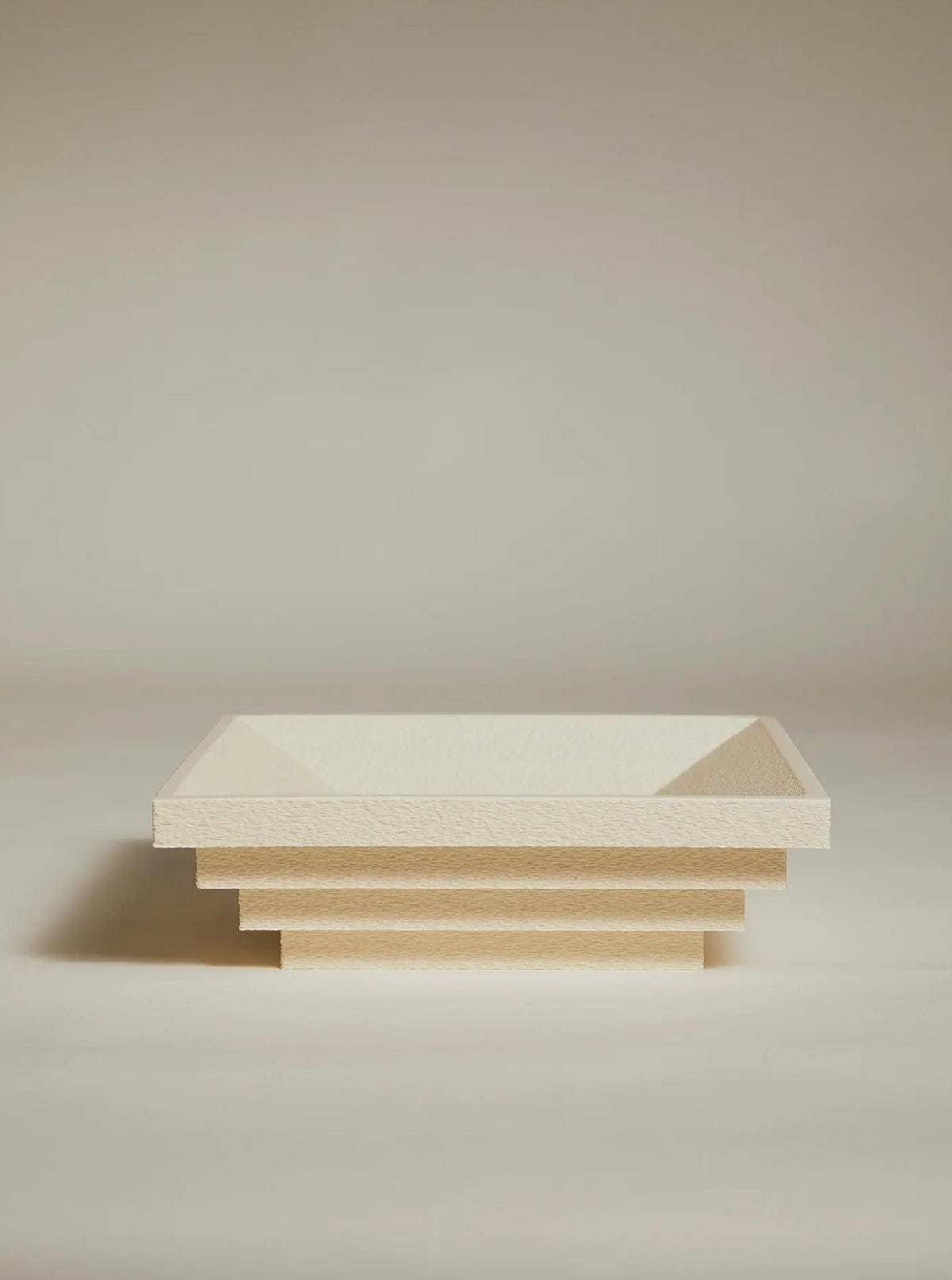The Bau Bowl by Argot Studio is a minimalist, cream-colored sculptural piece featuring tiered rectangular forms and a stepped design on a textured surface, set against a plain background, offering luxury appeal as elegant interior decor.