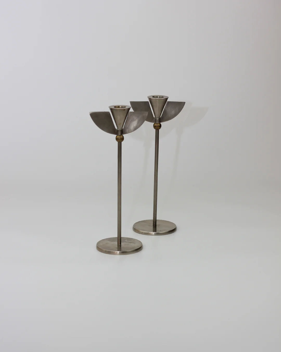 The Memphis Candleholders 80s by Boga Avante Shop feature two stainless steel candleholders with a modern inverted cone design, slender stems, and round bases. Reminiscent of sleek Memphis Milano lines, they're set against a plain white background.