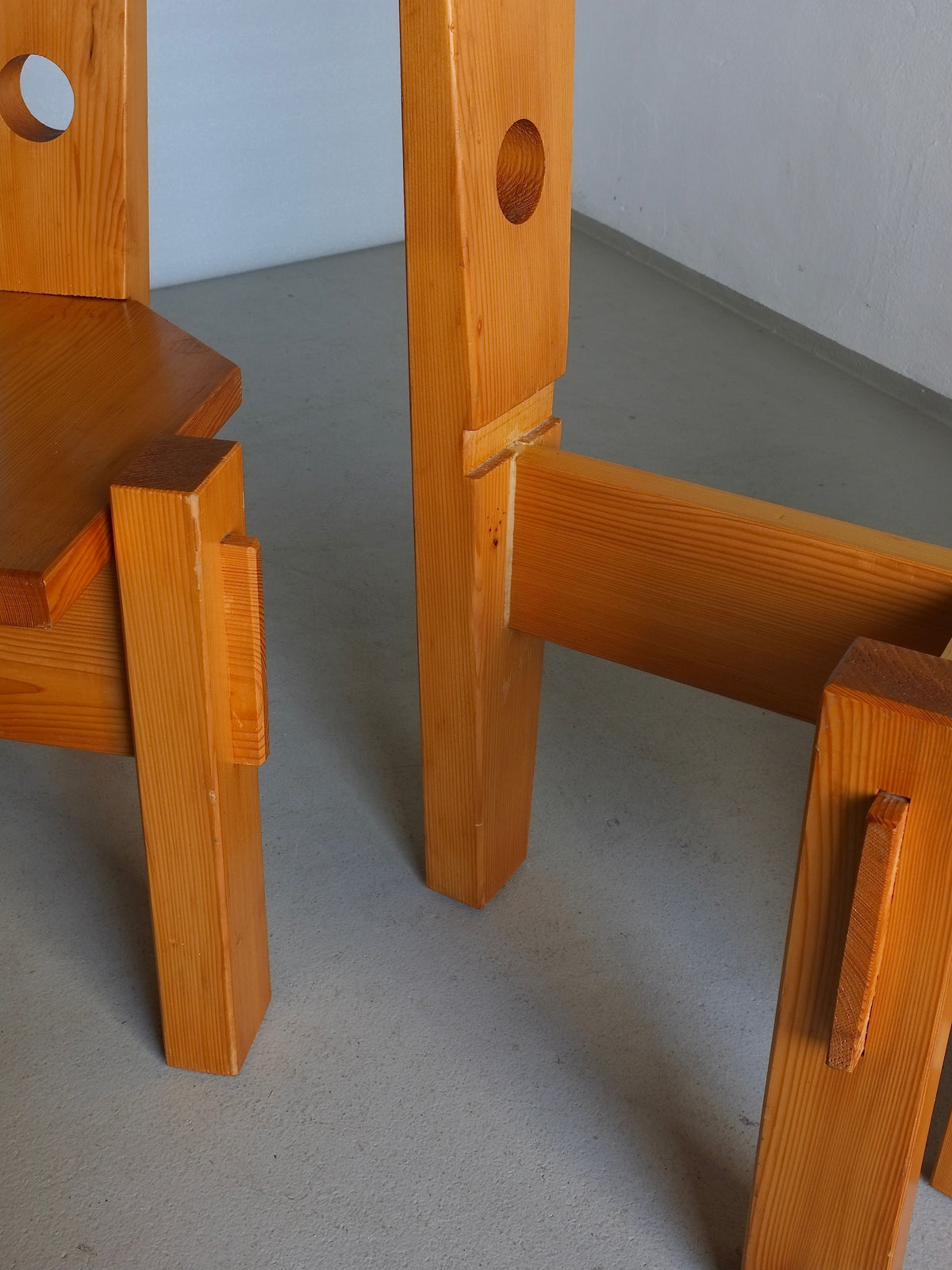 Close-up of 4 sculptural pine chairs by Erwin Egel, 1960s design for Veter Vintage, showcasing distinctive geometric style with thick, angular legs and visible wooden joints. Circular cutouts on sides complement the light gray floor and off-white wall background.