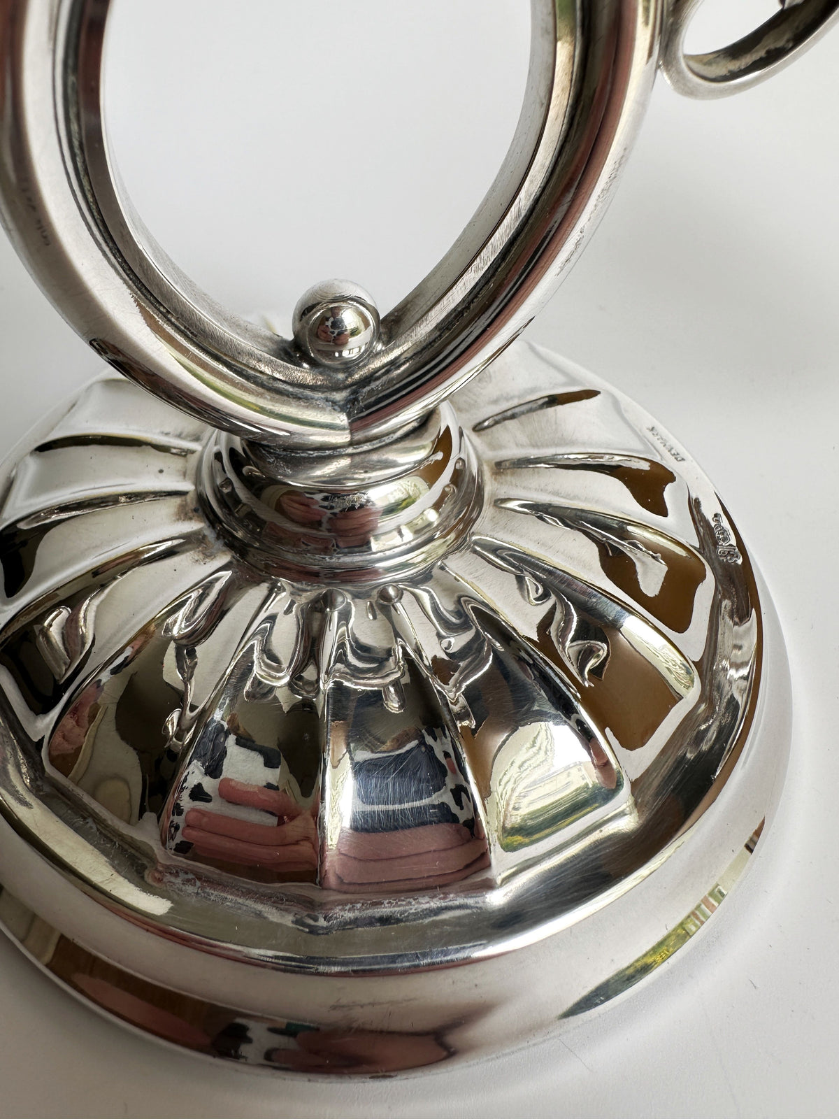 Close-up of the Danish Mid Century Candleholder by Dodo Vintage, featuring a polished, silver-colored metal base with a decorative grooved design. The shiny, reflective surface elegantly reveals subtle reflections of its surroundings against a smooth, light background.