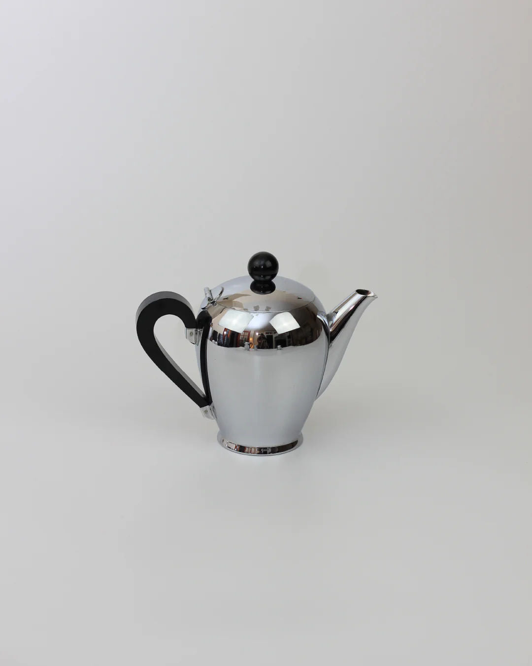The Italian Coffee and Tea Set, 1945 by Boga Avante Shop features a shiny silver teapot with a black handle and knob, reflecting mid-20th century craftsmanship, displayed on a plain, light gray background.