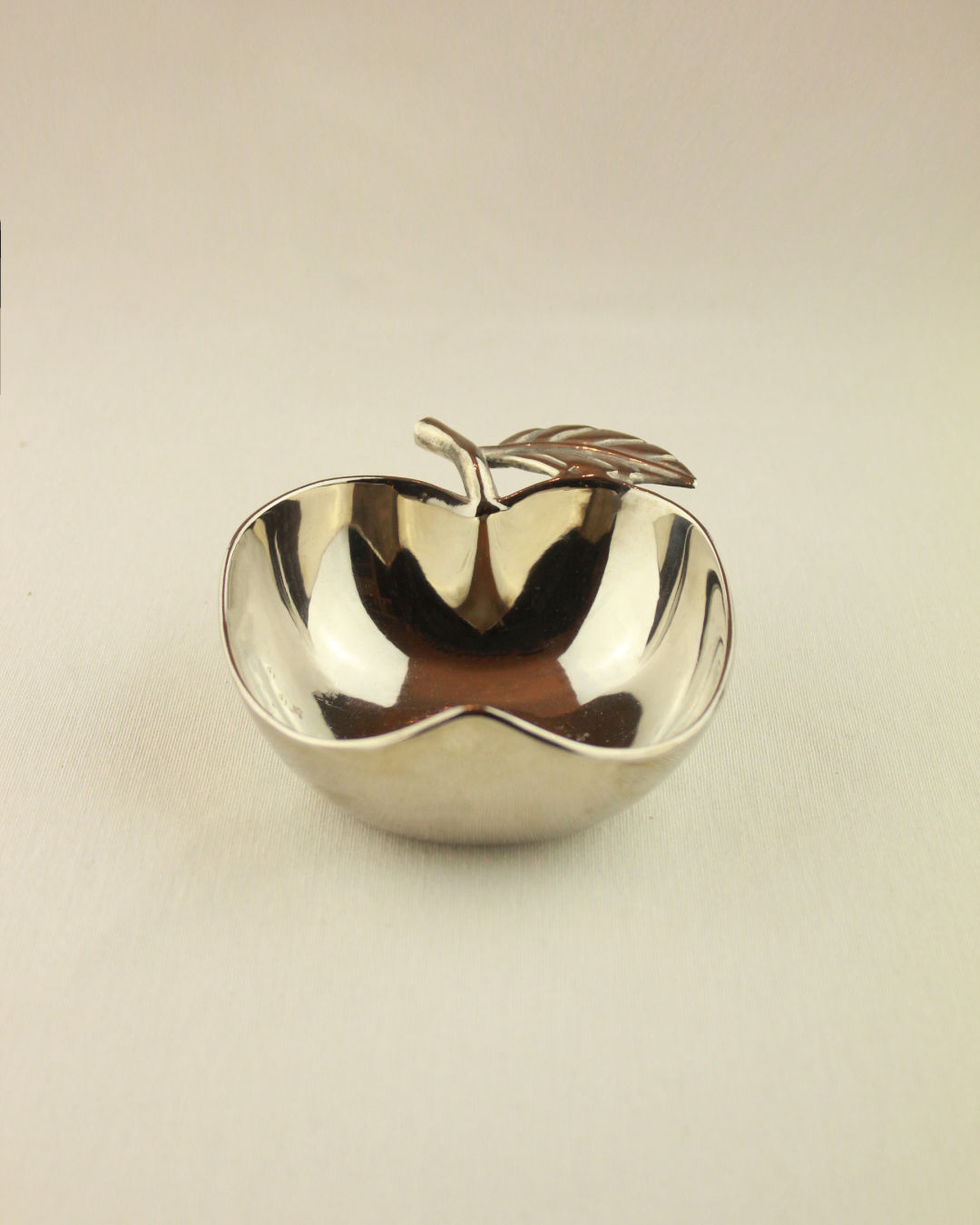 The Decorative Apple Shaped Dish by Boga Avante Shop is a small, shiny silver bowl with a metallic stem and leaf detail, ideal as a serving bowl, shown on a plain light background.