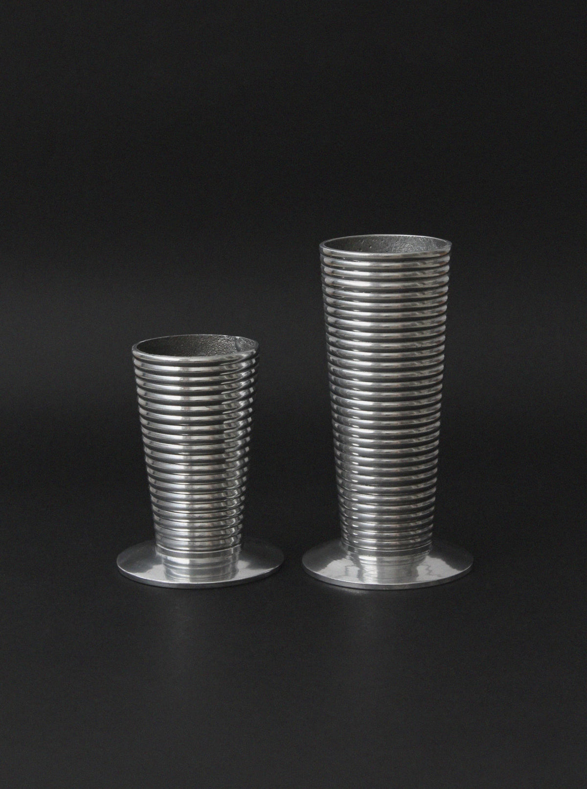 Two ribbed aluminum vases in different heights on dark background