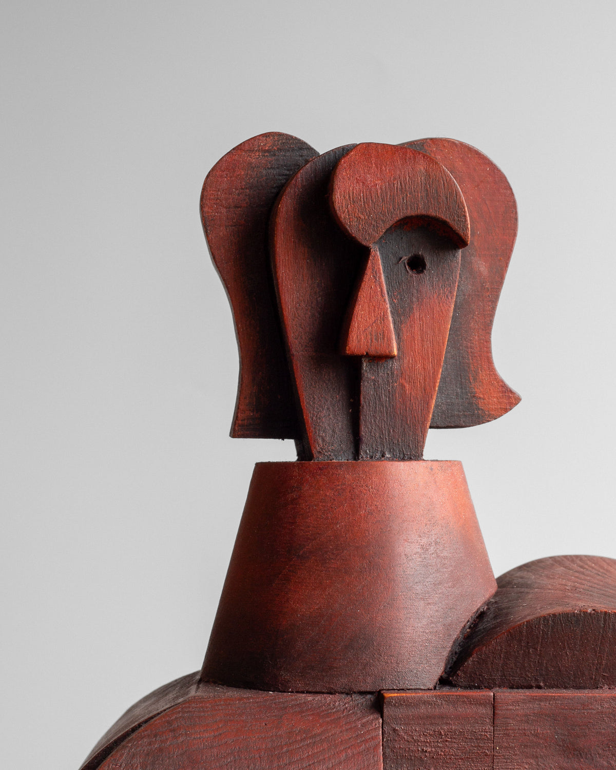 The Vintage Cubist Sculpture II by Atelier Boulogne from Spigel showcases a geometric, stylized female figure with elongated, reddish-brown shapes and a cylindrical neck, creating a cubist wooden art piece against a plain gray background.