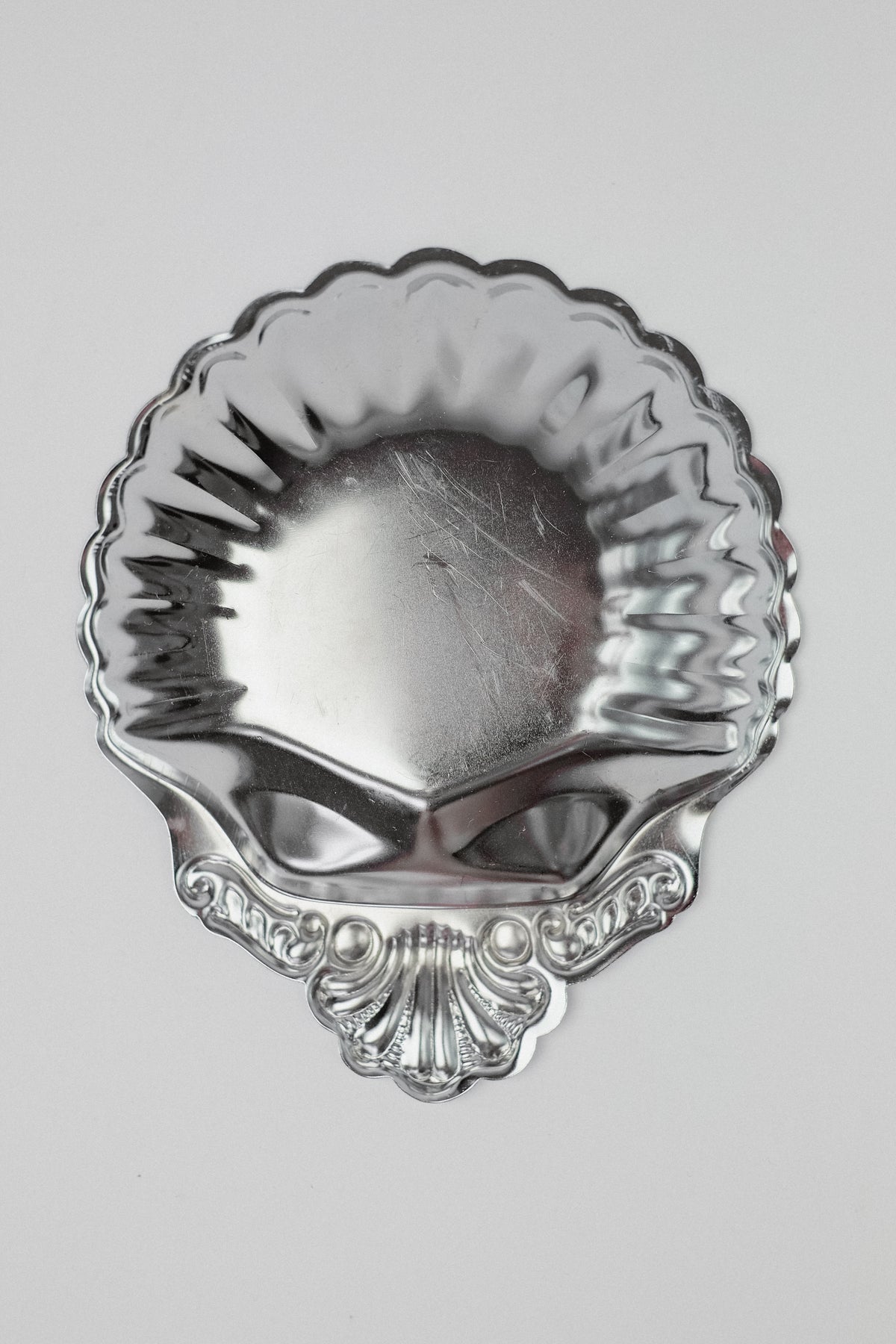 A vintage set of 6 small silver, scallop-shaped dishes by septembre studios features intricate edge designs and is showcased in beautiful detail against a plain white backdrop.