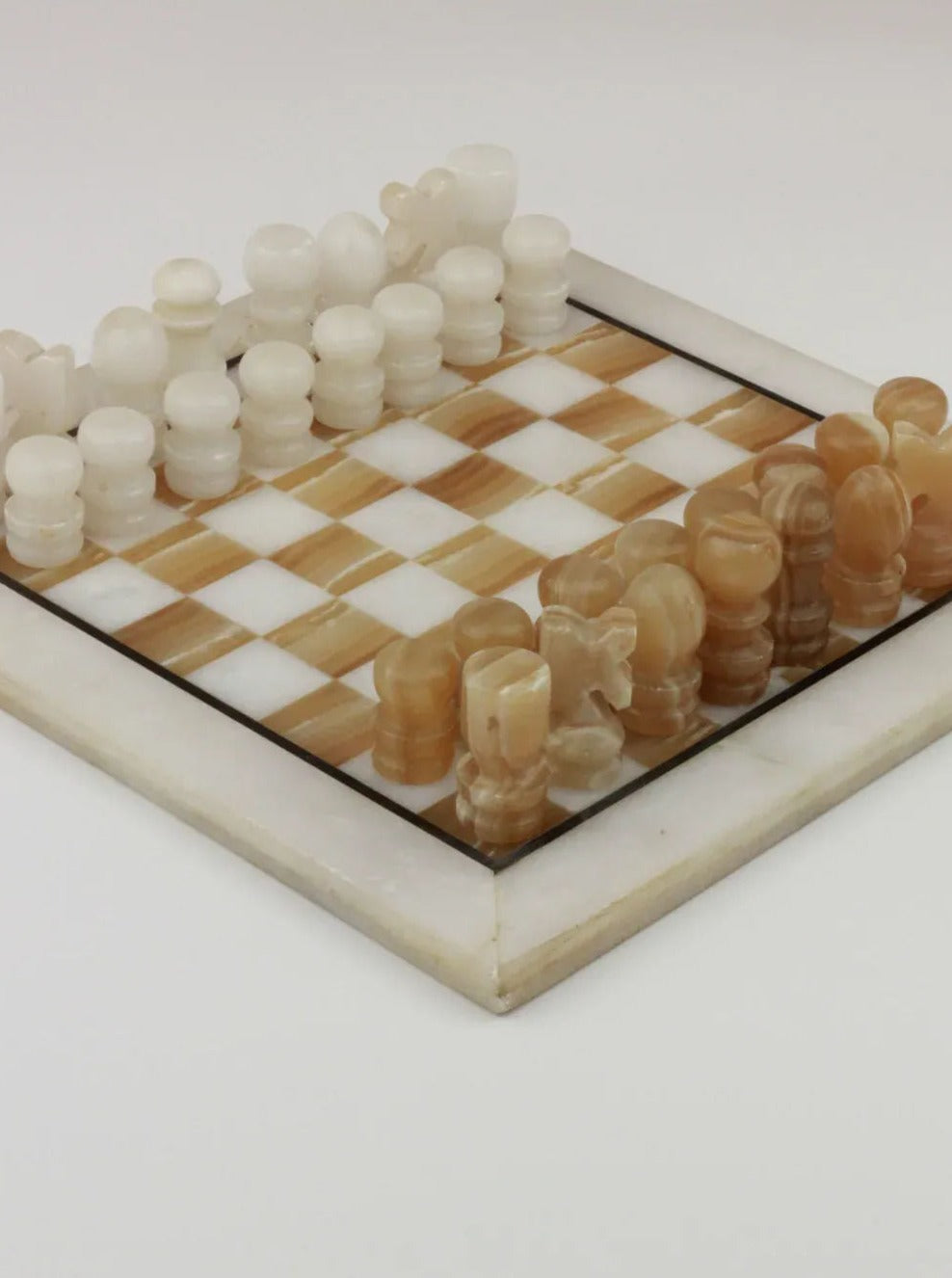 An onyx chess set featuring a light beige and white checkered board, with hand-carved pieces in beige on one side and white on the other. The pieces are neatly arranged for a new game. The Vintage Marble Chessboard from Boga Avante Shop has a polished, smooth finish.