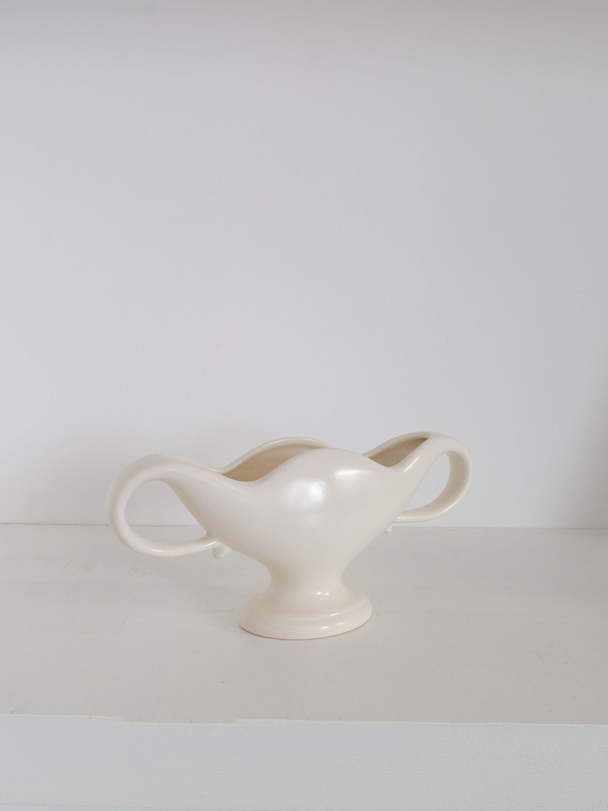The Mini Mantle Vase 1930s from Collection apart is a cream-colored, wavy-edged ceramic vase with two large handles on either side, standing on a white surface against a plain white background. This vintage vase features a glossy finish and symmetrical design with a pedestal base, reminiscent of classic Fulham Pottery styles by William J Marriner.