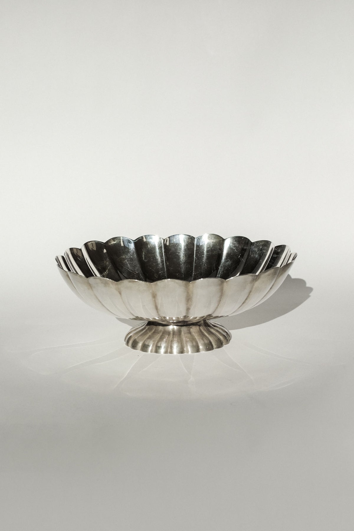 A silverplated centerpiece by septembre studios with a shiny, scalloped edge and fluted base is displayed on a plain light background.
