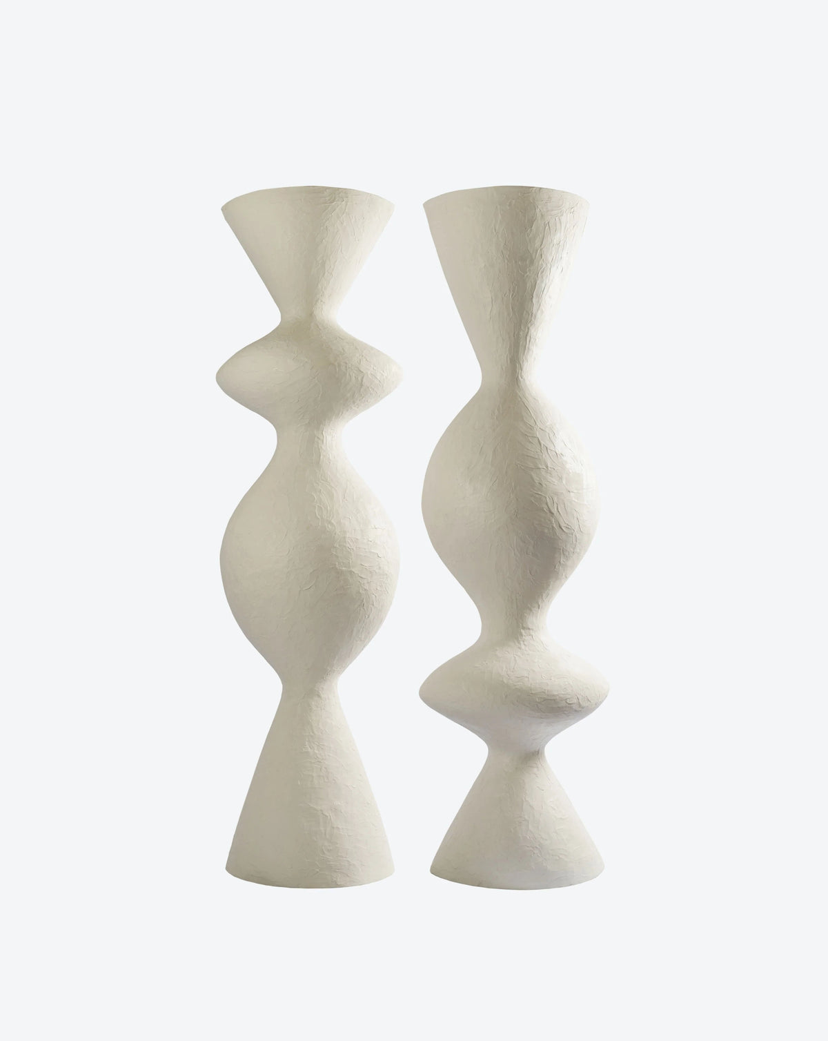 Against a light background, two tall, abstract "Venus II" floor lamps by Ransom & Dunn stand side by side. Handmade in Portugal, these white ceramic sculptures feature a textured surface and boast curvy, hourglass shapes with symmetrical bulges that echo the elegance of an uplighter lamp.