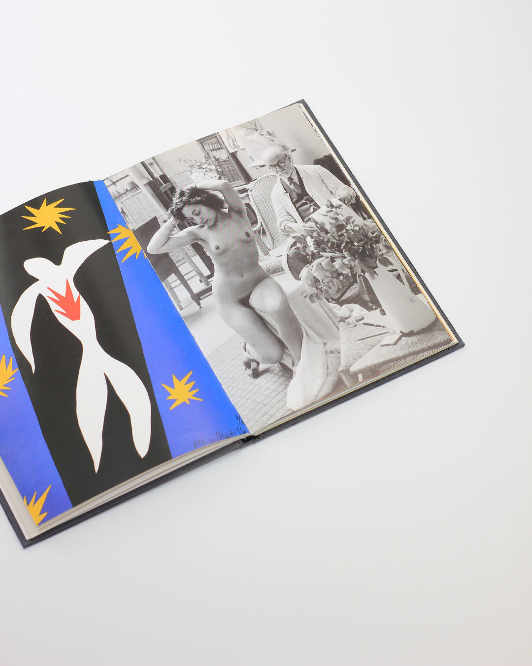 The 'Matisse in Nice' book from Boga Avante Shop is open to a vibrant abstract artwork with a white figure, Matisse-style, on the left, and a black-and-white photo of a nude woman and a clothed figure on the right, all on a plain white background.
