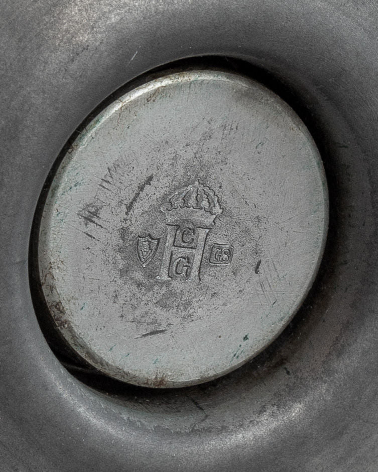 Close-up of 1930s Modernist Candleholders by Sylvia Stave for Spigel, showcasing engraved markings with a crown and letters around three shields. The metal resembles modernist works, featuring a circular indentation with a slightly worn look.