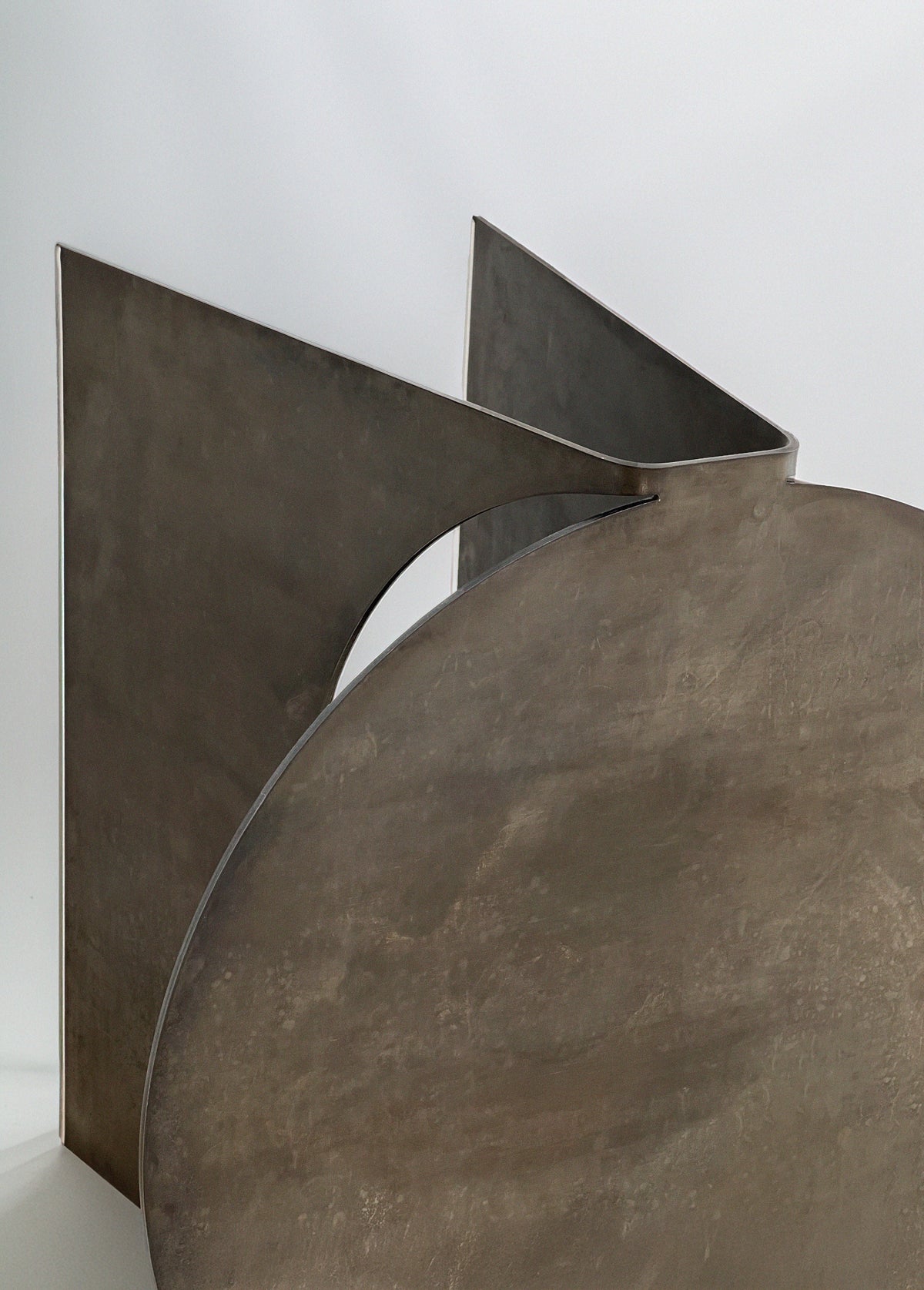 The 'Maru' Side Table by Modan features a large circular steel form intersected by angled planes, all in a smooth matte metallic finish, creating a modern abstract look and making it a unique accent piece.
