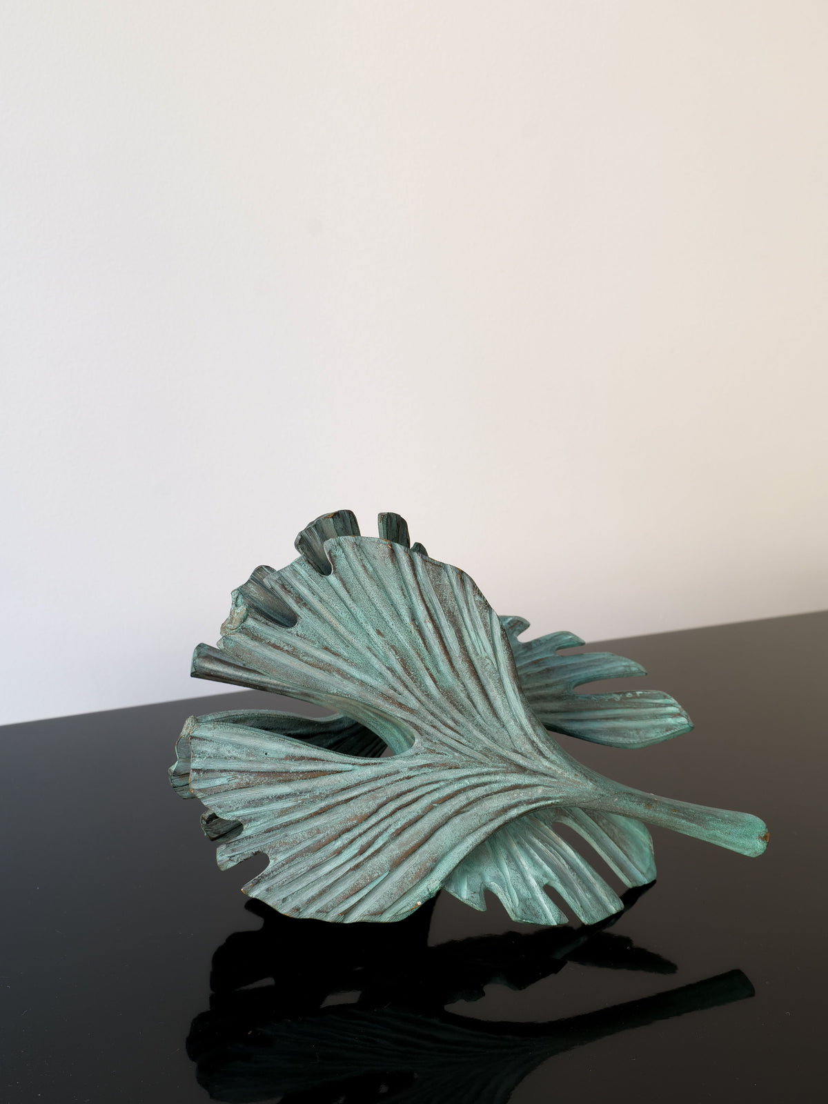 The Bronze Ginko Biloba Sculpture by Collection apart features a textured, teal leaf with detailed veins on a glossy black surface against a plain white background. Its slightly metallic sheen adds depth and interest to its organic form.
