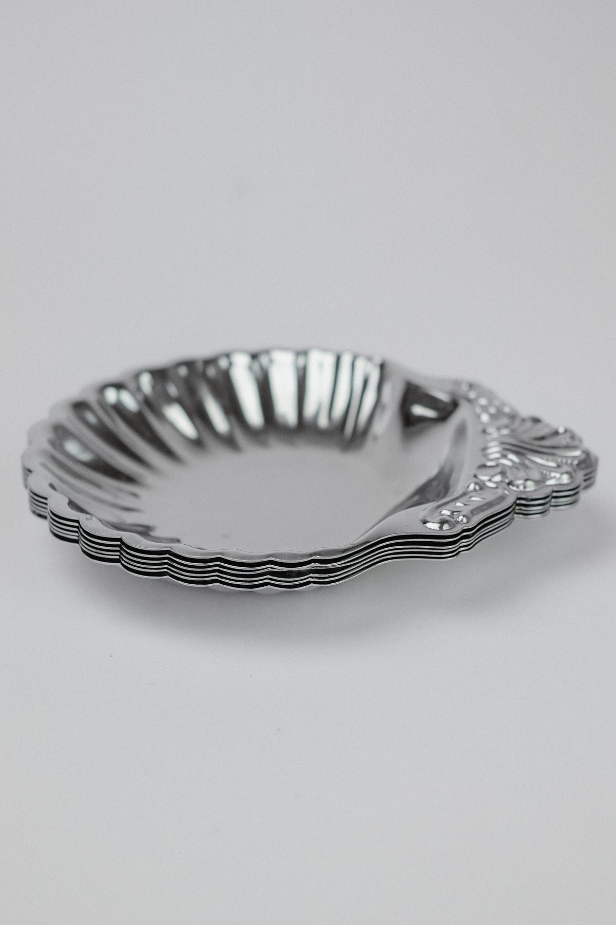 The Set of 6 Small Shell Dishes by septembre studios features silver decorative plates with scalloped edges and an ornate handle. Each plate, in vintage condition, has a shiny, reflective surface against a plain white background and unique character.