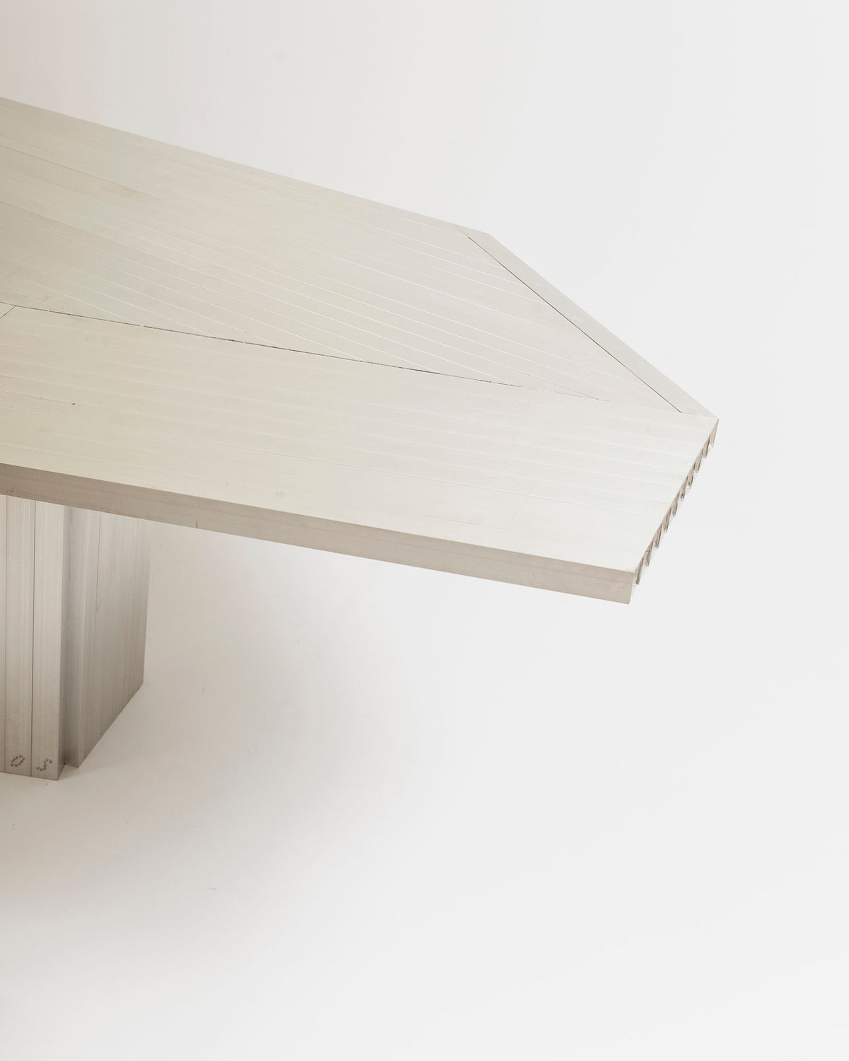 A close-up of the Aluminum Dining Table by Studio HAOS highlights its minimalist geometric edges and lightly brushed finish, set against a white background, exemplifying refined contemporary design.