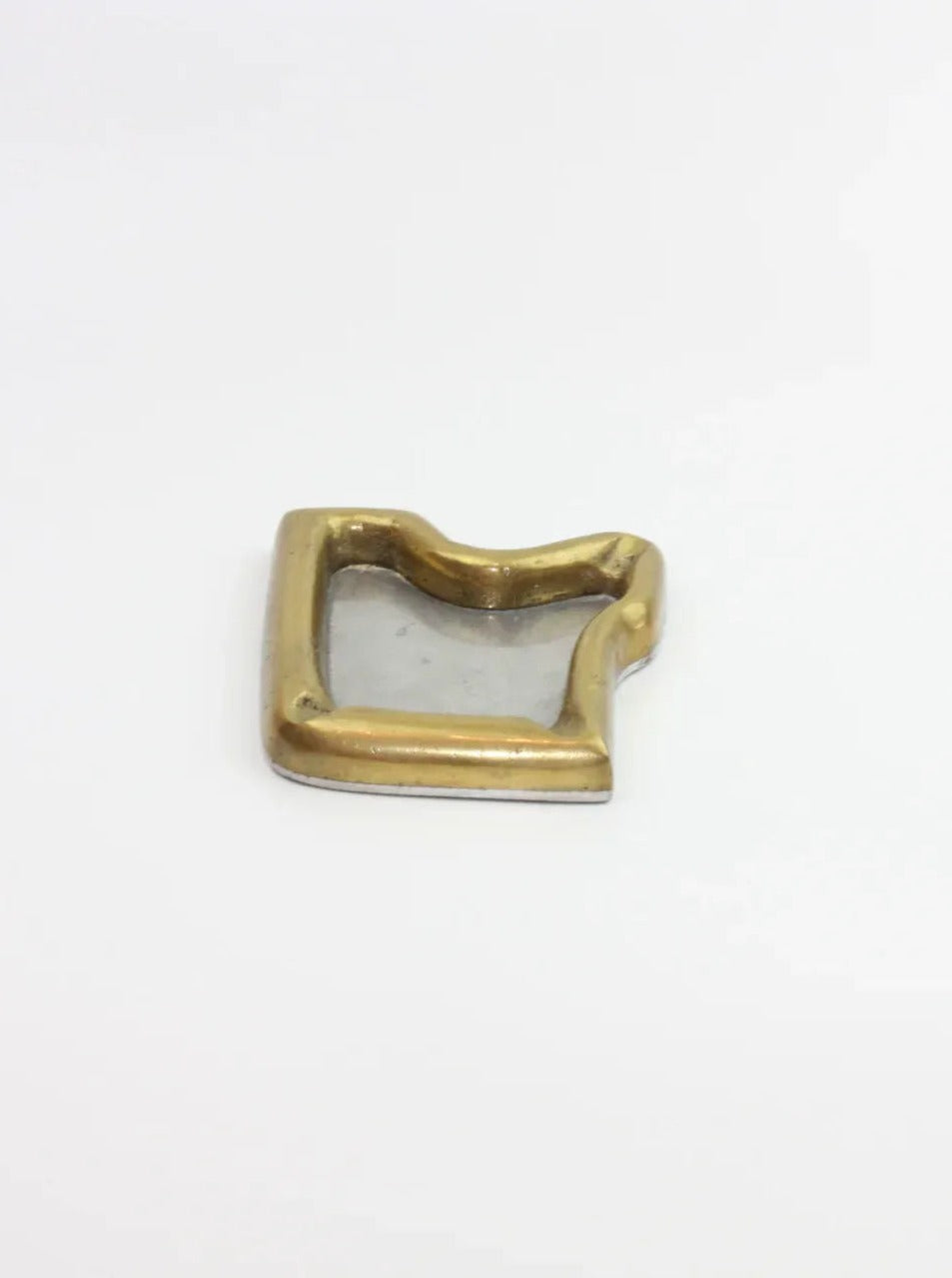 A brass and silver square-shaped vintage item with a wavy, uneven border sits on a plain white surface. The brass forms the outer edge, while the silver fills the center, embodying a Brutalist style reminiscent of mid-century design. This is the Brutalist Ashtray from Boga Avante Shop.