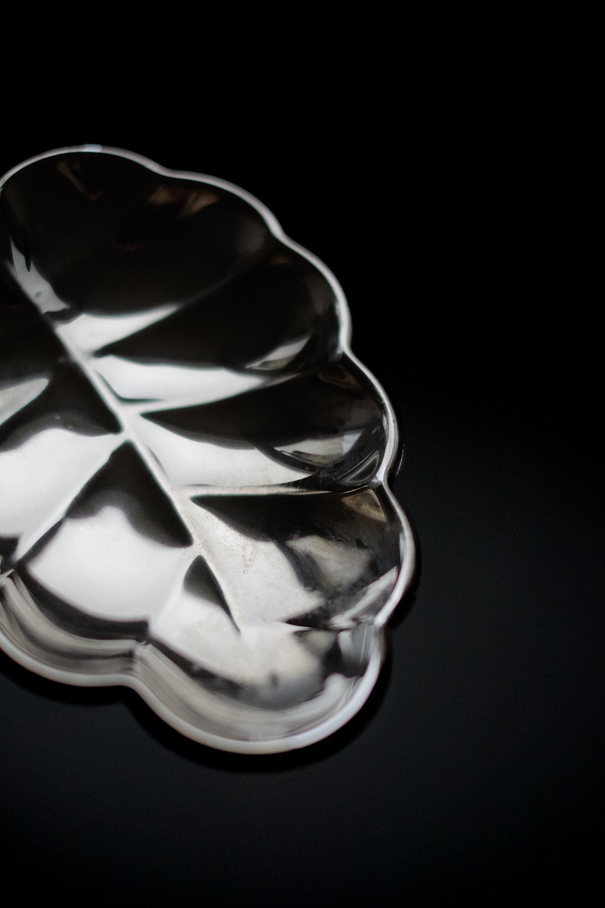 The septembre studios Serving Dish Leaf exudes vintage charm with its shiny silver hue and intricate vein details. Placed on a black surface, highlights accentuate its elegant contours.