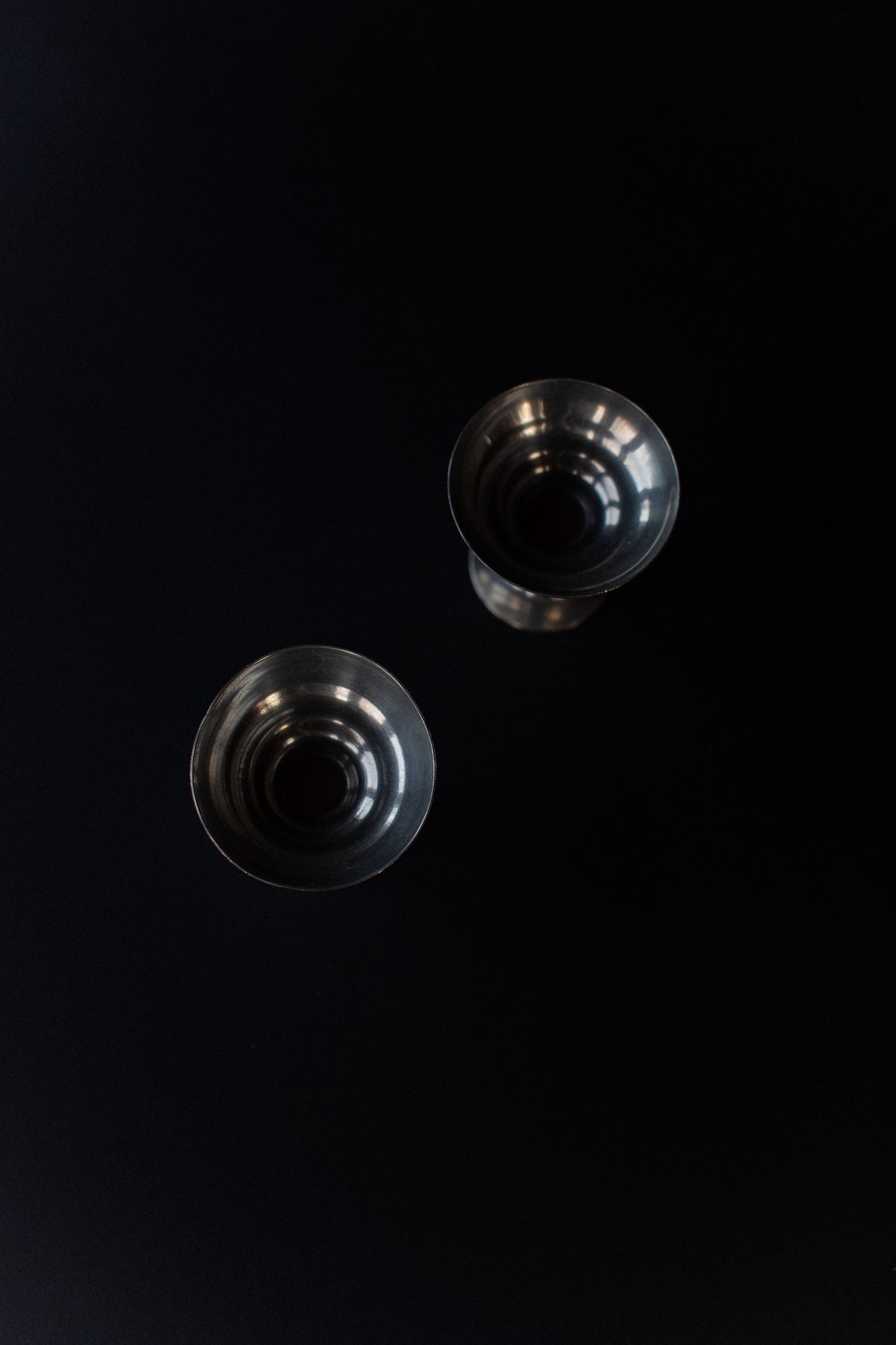 From above, two metallic Out For Lunch Ice Cream Cups rest diagonally on a black surface. Their Art Deco design and vintage style are highlighted by light reflecting off their rims and interiors.