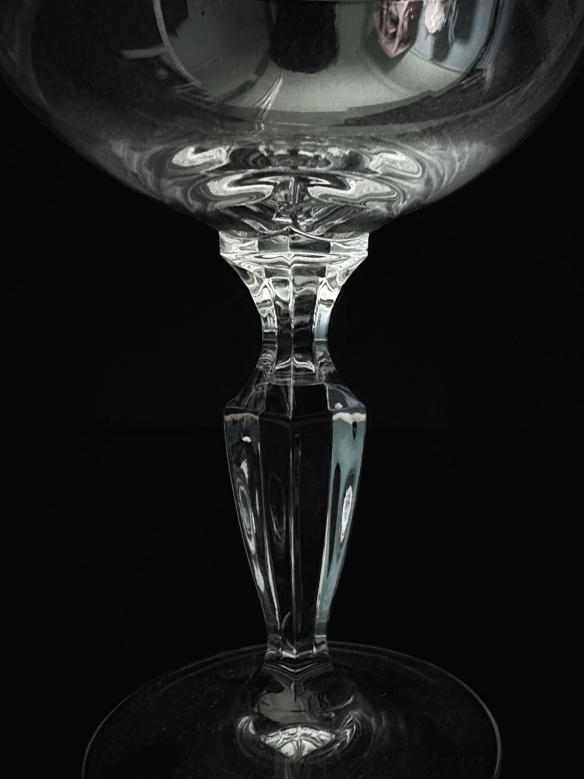Close-up of the stem of a Dodo Vintage crystal champagne coupe from the 6 Mid Century Crystal Champagne Coupes set against a black background. Reflections of light highlight its elegant design and smooth surface, creating a sense of symmetry and delicacy reminiscent of mid-century craftsmanship.