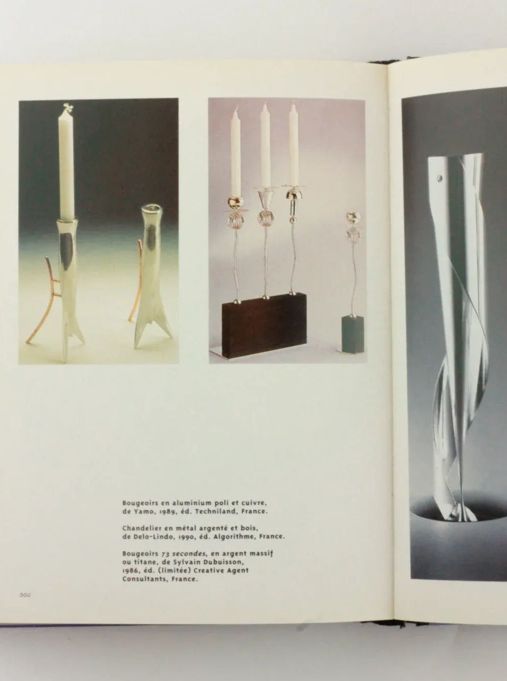 An open Objets Affectifs: Le Nouveau Design de la Table from Boga Avante Shop displays photos of various modern candleholders. On the left page, there are three candleholders: two minimalistic designs and one more intricate. The right page showcases a sleek, twisted metal candleholder with distintivo diseño italiano. Text descriptions are below each image.