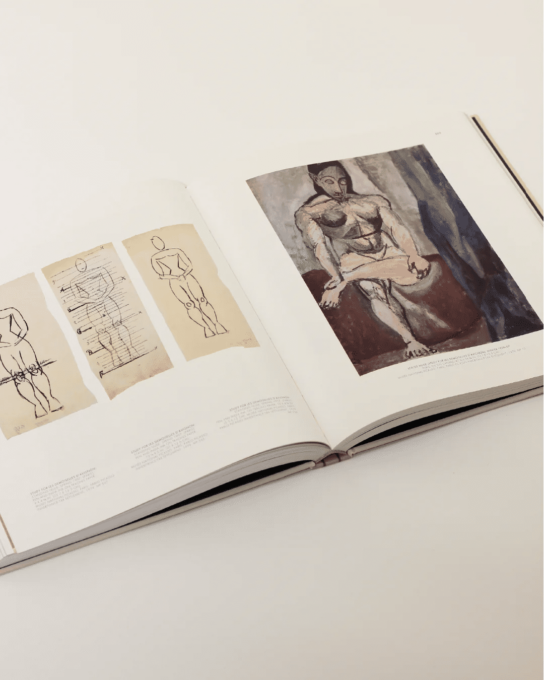 The Cubist Picasso Book from Boga Avante Shop is opened to reveal pages of sketches and a painting. On the left page, anatomical studies are on display, while the right page features a Cubist portrait of a seated figure inspired by Picasso. This artistic exploration lies gracefully on a light surface.