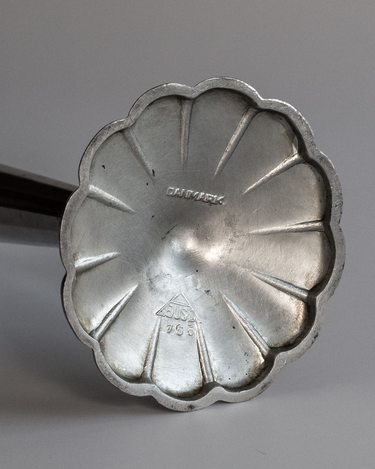 A metallic flower-shaped waffle iron head marked "DENMARK" exudes Scandinavian elegance, with a triangular text emblem reminiscent of Just Andersen craftsmanship, set against a light gray gradient.
