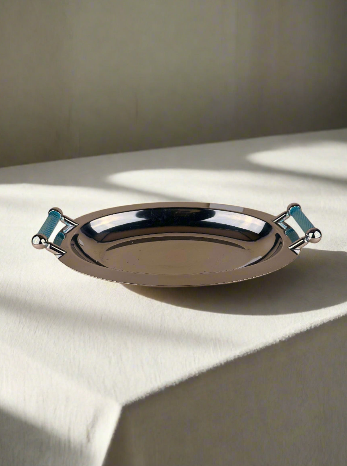 A polished silver-coloured Dodo Vintage Italian 1980s Tray with azure blue handles on either side is placed against a neutral beige background. The ribbed texture of the handles adds a touch of style to the sleek, reflective surface, evoking an elegant piece from Italy 1980s.
