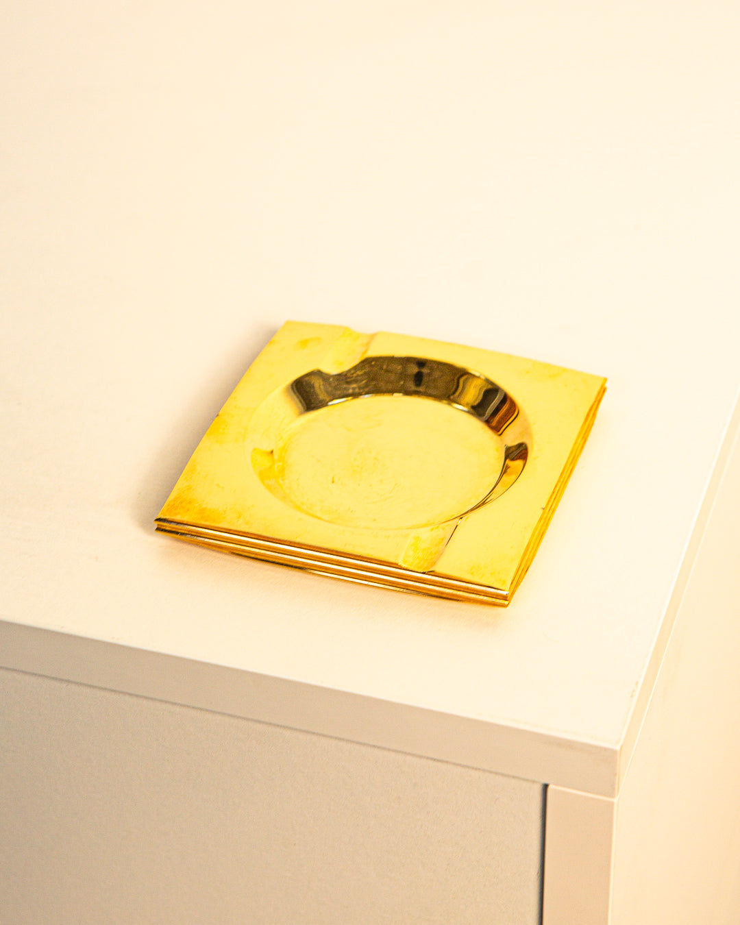 The Brass Ashtray by Francois Gross 60's from Treaptyque sits on a white table, its shiny brass surface reflecting light in classic 60s style.