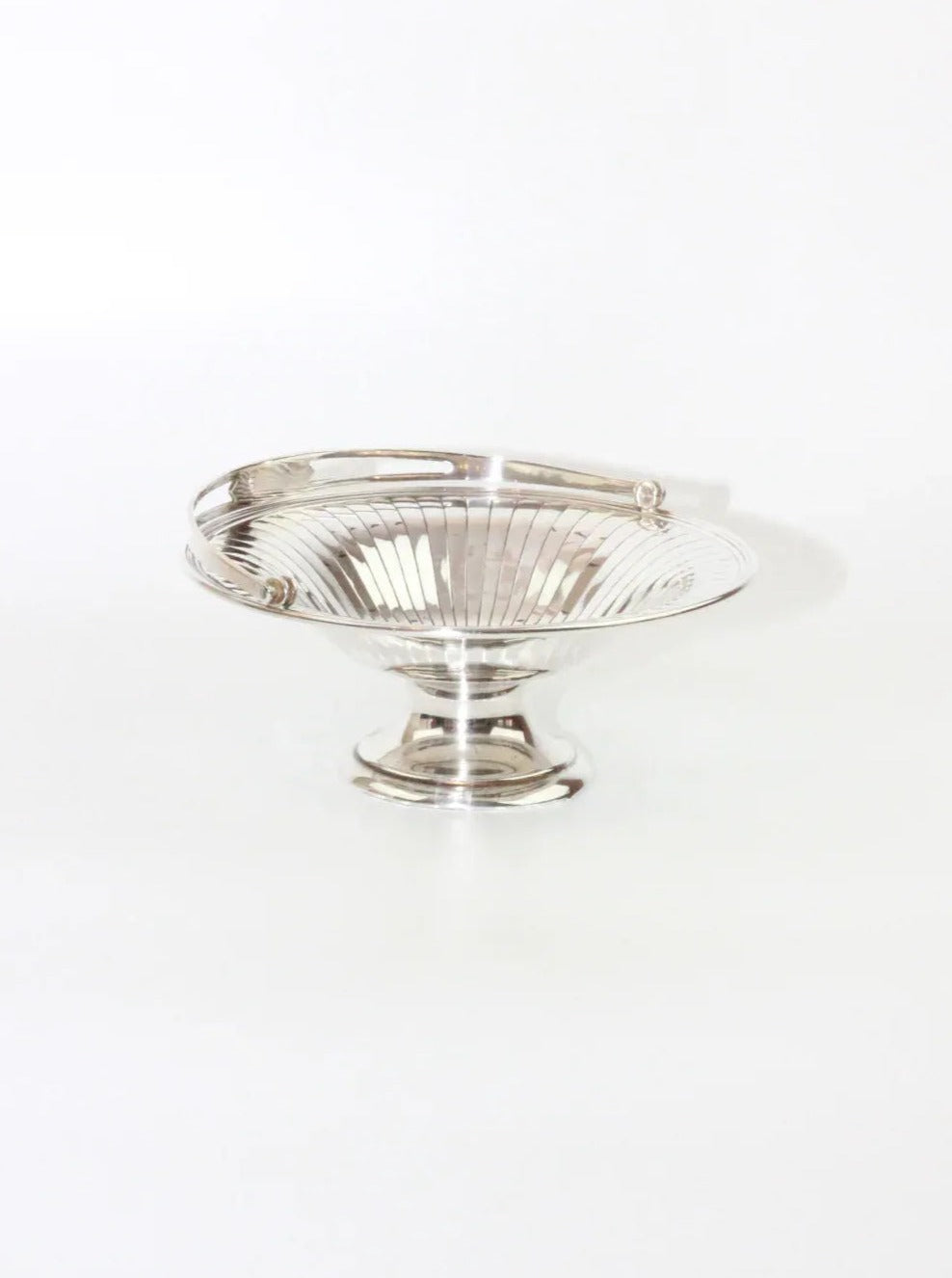 The Boga Avante Shop’s Silver Fruit Bowl is a round pedestal bowl crafted from nickel silver, showcasing a flared, ribbed design and adorned with two small, looped handles on the sides. This decorative piece has a polished, reflective surface and is elegantly set against a plain white background.