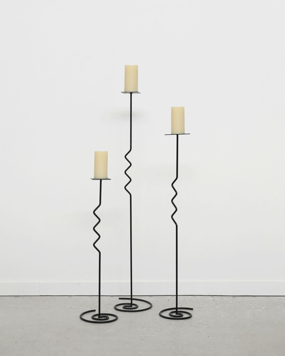 Set of three black metal spiral floor candleholders with cream candles