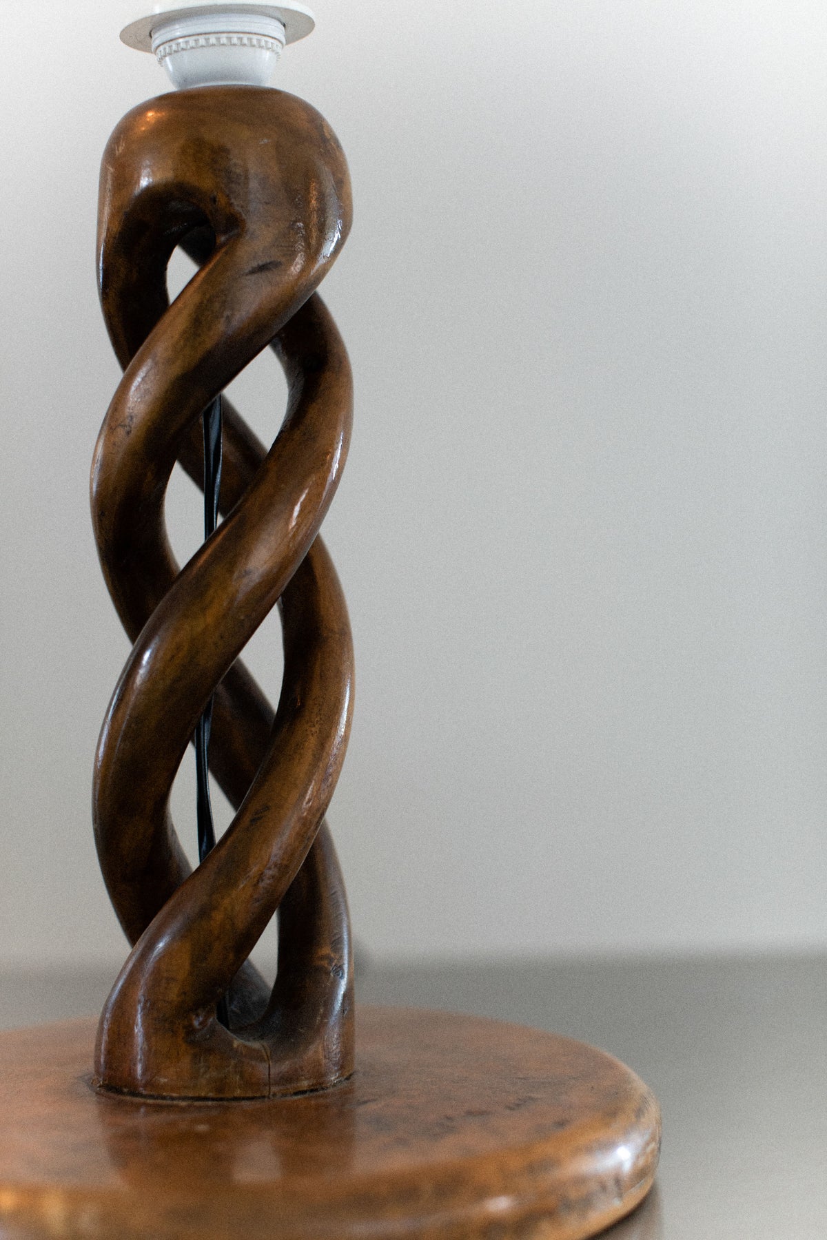 A close-up of the Early-Century Lamp by Out For Lunch, featuring a meticulously handcrafted base with an intricately twisted wooden design resembling a double helix. It is set against a neutral background, with the lamp socket visible at the top yet no bulb attached.