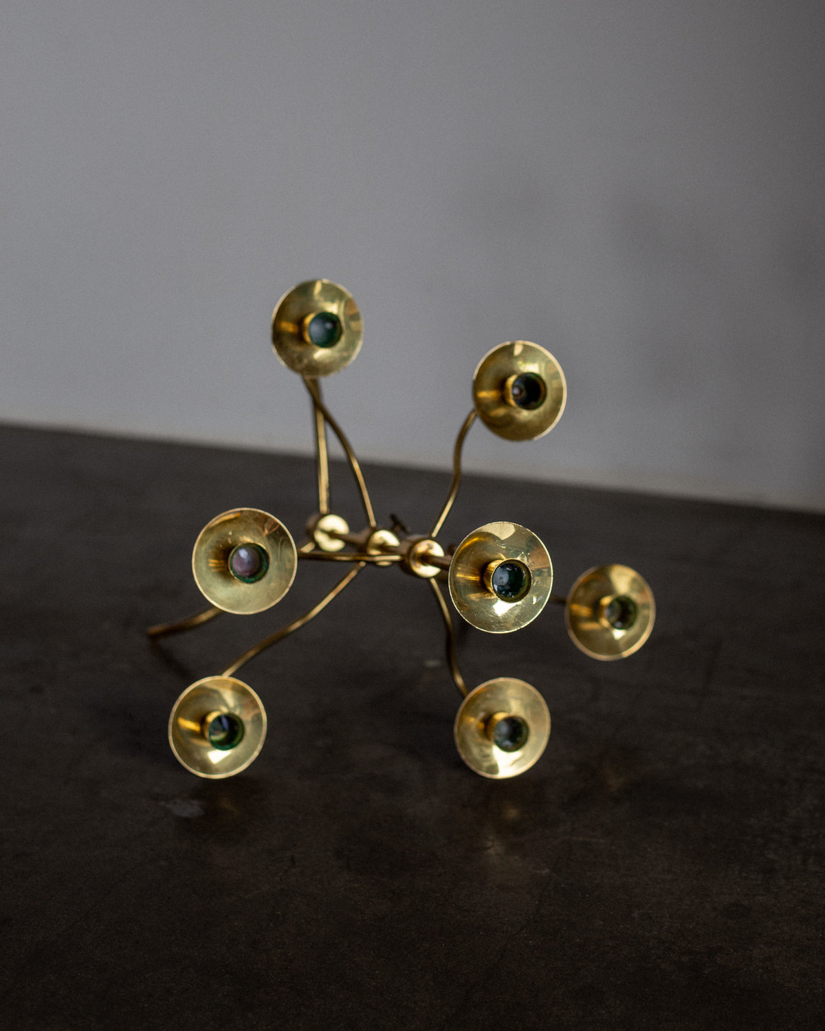The Swedish Mid-Century Brass Candelabra by Spigel features interconnected rods with circular ends, each holding a small sphere. Reminiscent of Josef Frank's design, its Scandinavian Modern style is highlighted against a dark, simple background.