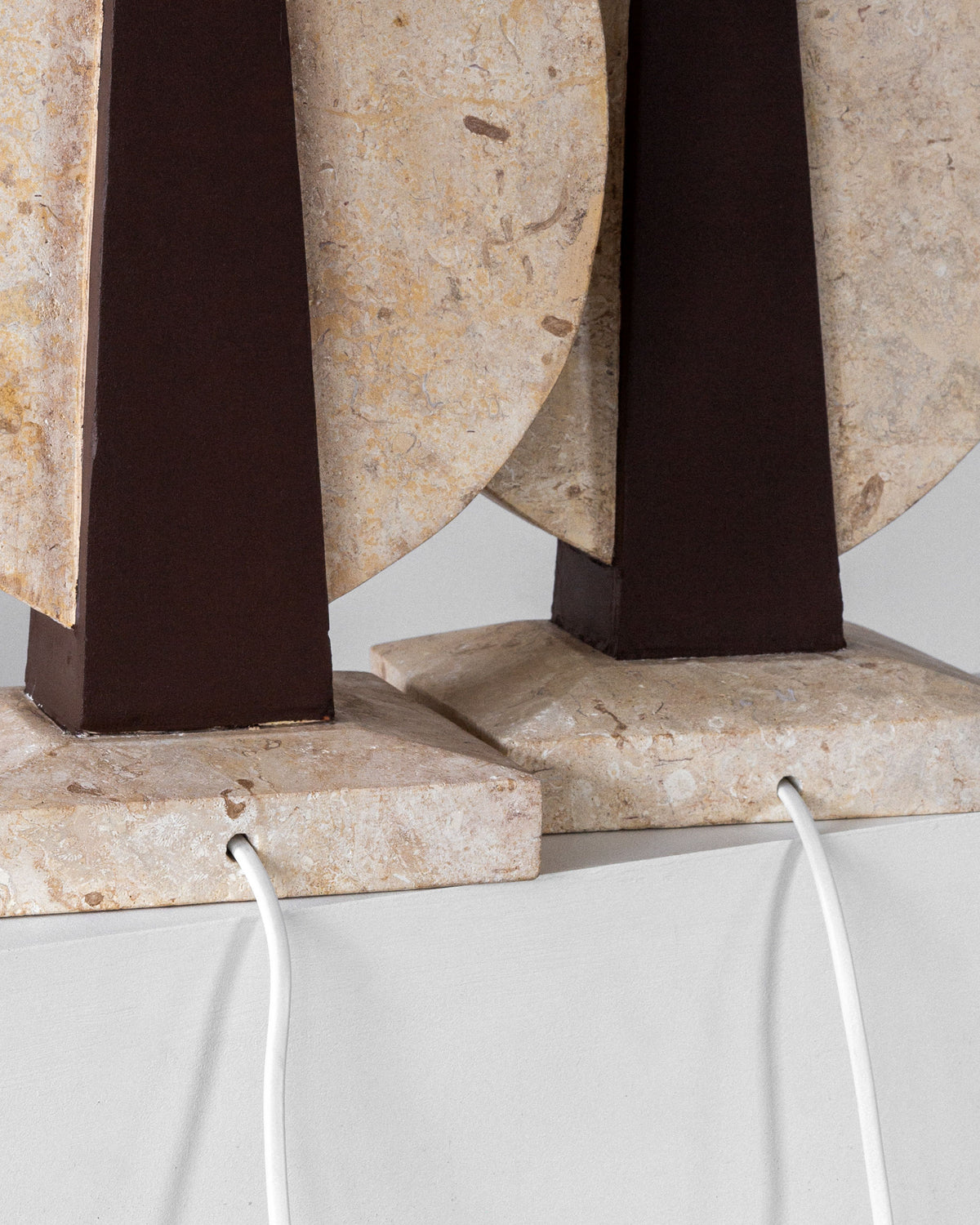Close-up of two Spigel 1970s table lamps, featuring rectangular dark brown bodies and semi-circular beige stone accents. Each elegant lamp stands on a travertine base with a white cord, capturing timeless design. Product: Pair of Large Travertine Table Lamps by Spigel.