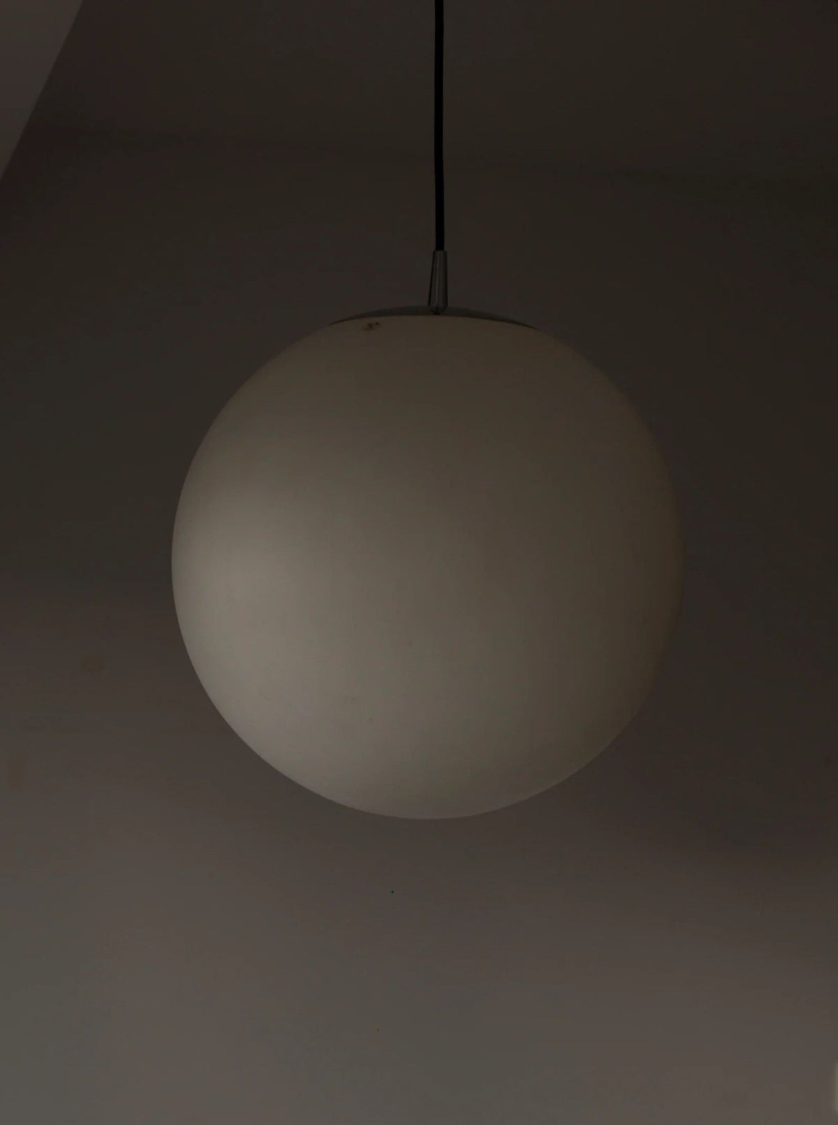 A large, spherical Glass Globe Lamp Peill & Putzler by CU-RA-TED in vintage condition hangs from a black cord against a plain, dark background. The lamp is mostly unlit, creating a shadowy, minimalistic appearance.