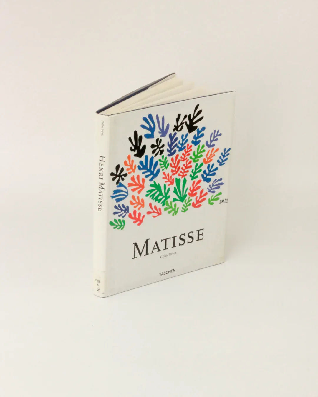 A hardcover book by Boga Avante Shop titled "Henri Matisse Vintage Book - Illustrated Publication" stands upright against a plain background. The cover is adorned with colorful, gouache cut-outs arranged in clusters, reflecting Henri Matisse's modern art style. The author's name, Gilles Néret, is printed on the spine.