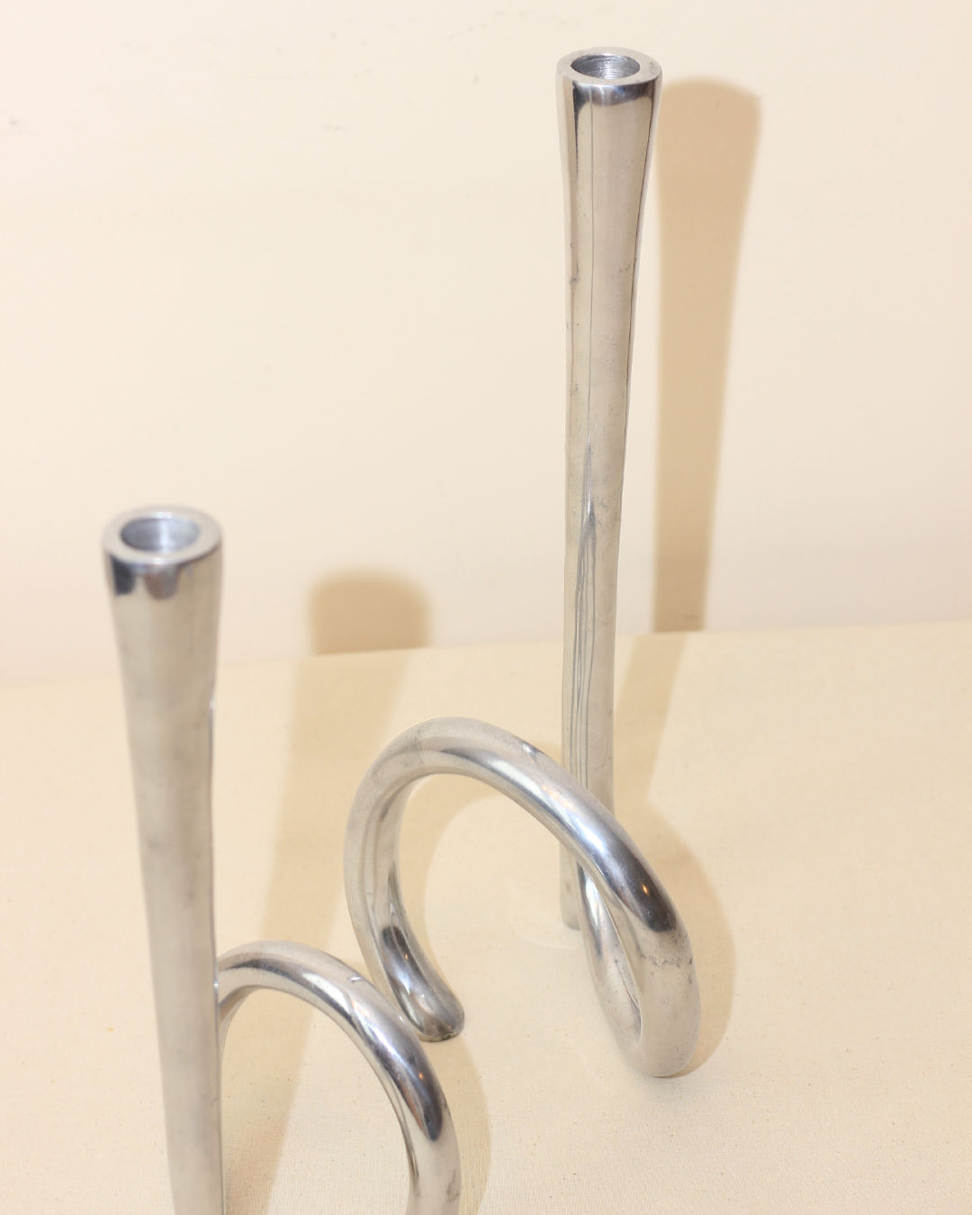 The Cast Aluminum Candleholders from Boga Avante Shop feature a modern, minimalist design—one upright, one with a half-circle curve—evoking 1980s style and making them a striking accent for contemporary decor.